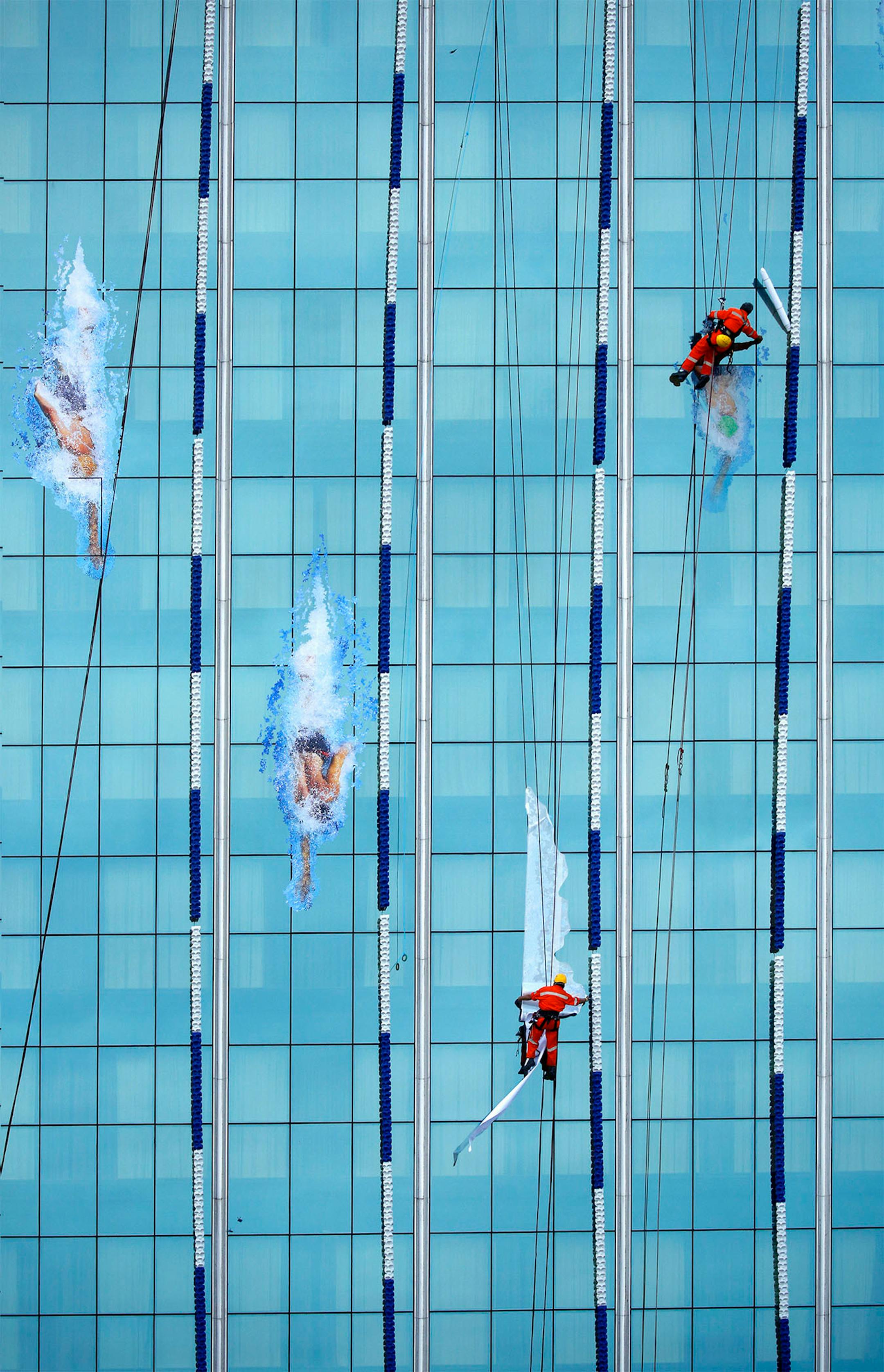 Crews rappelling from the roof of the Nissan building near Copacabana Beach, were installing a replica Olympic swimming pool on the side of the building to promote the summer games in Rio.