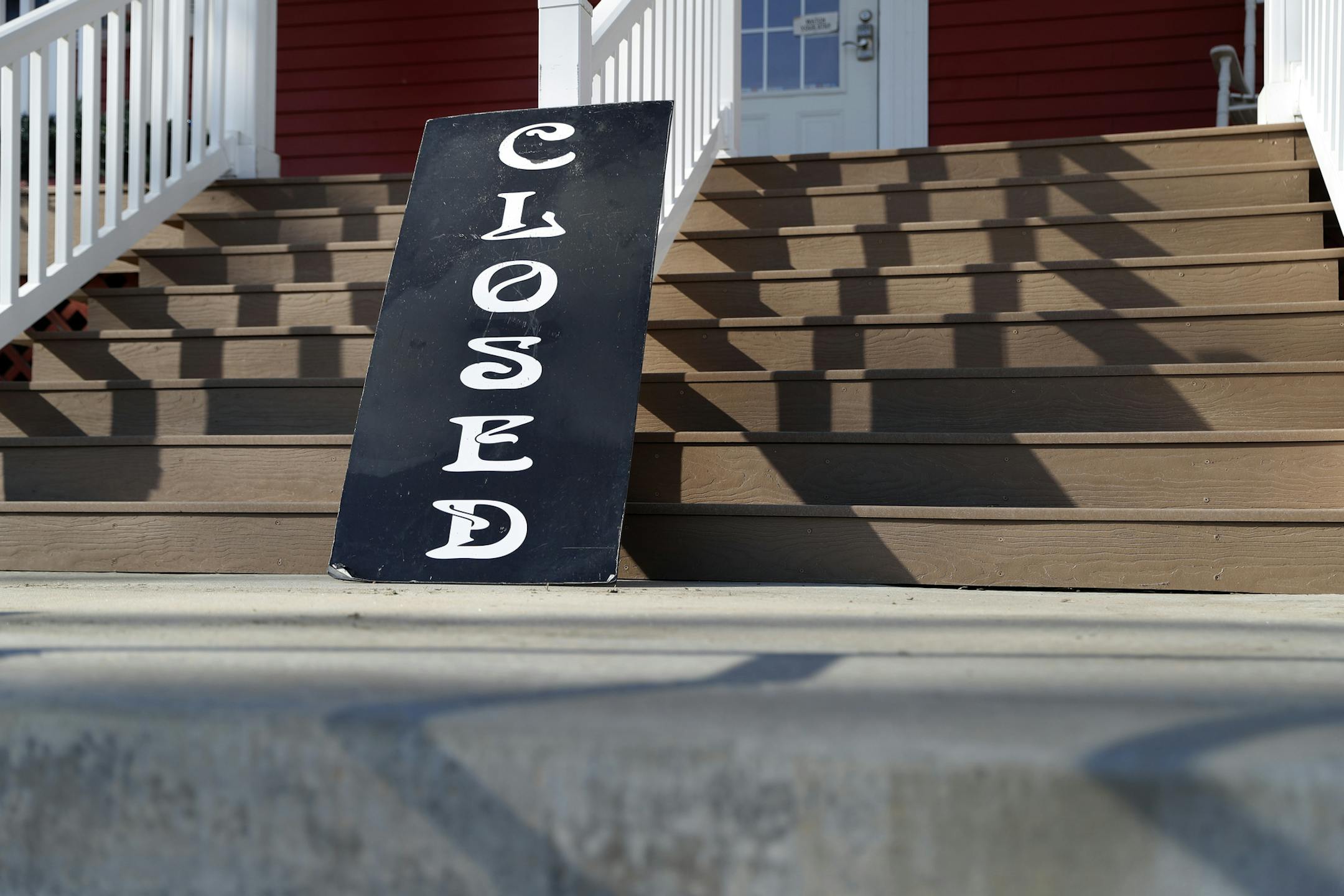 In this Tuesday, April 7, 2020 photo, a sign leans against the front steps of a closed business in Kimmswick, Mo. The coronavirus outbreak has brought stay-at-home orders and social distancing to the tiny town along the banks of the Mississippi River and has turned away the tourists it counts on to survive. (AP Photo/Jeff Roberson)