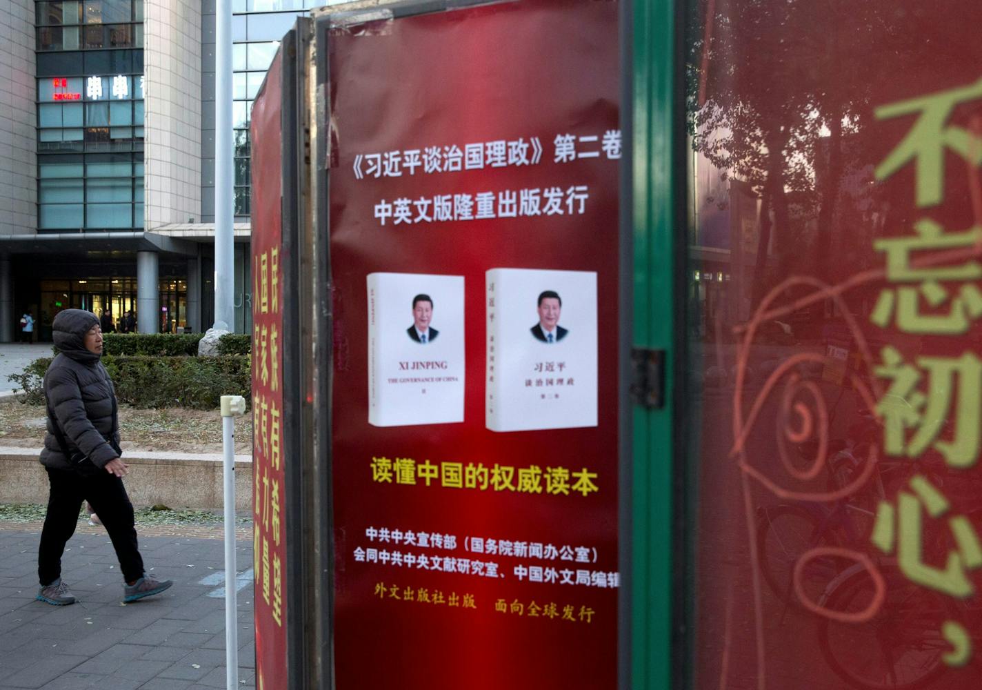 A resident walks past a newstand promoting a book titled "Xi Jinping, the Governance of China" near the government slogan "Don't forget your original intent" in Beijing, China, Wednesday, Nov. 22, 2017. At the start of his second five-year term as leader of China's ruling Communist Party, Xi is at the center of China's most colorful efforts to build a cult of personality since the death of the founder of the People's Republic, Mao Zedong, in 1976. (AP Photo/Ng Han Guan) ORG XMIT: XHG104