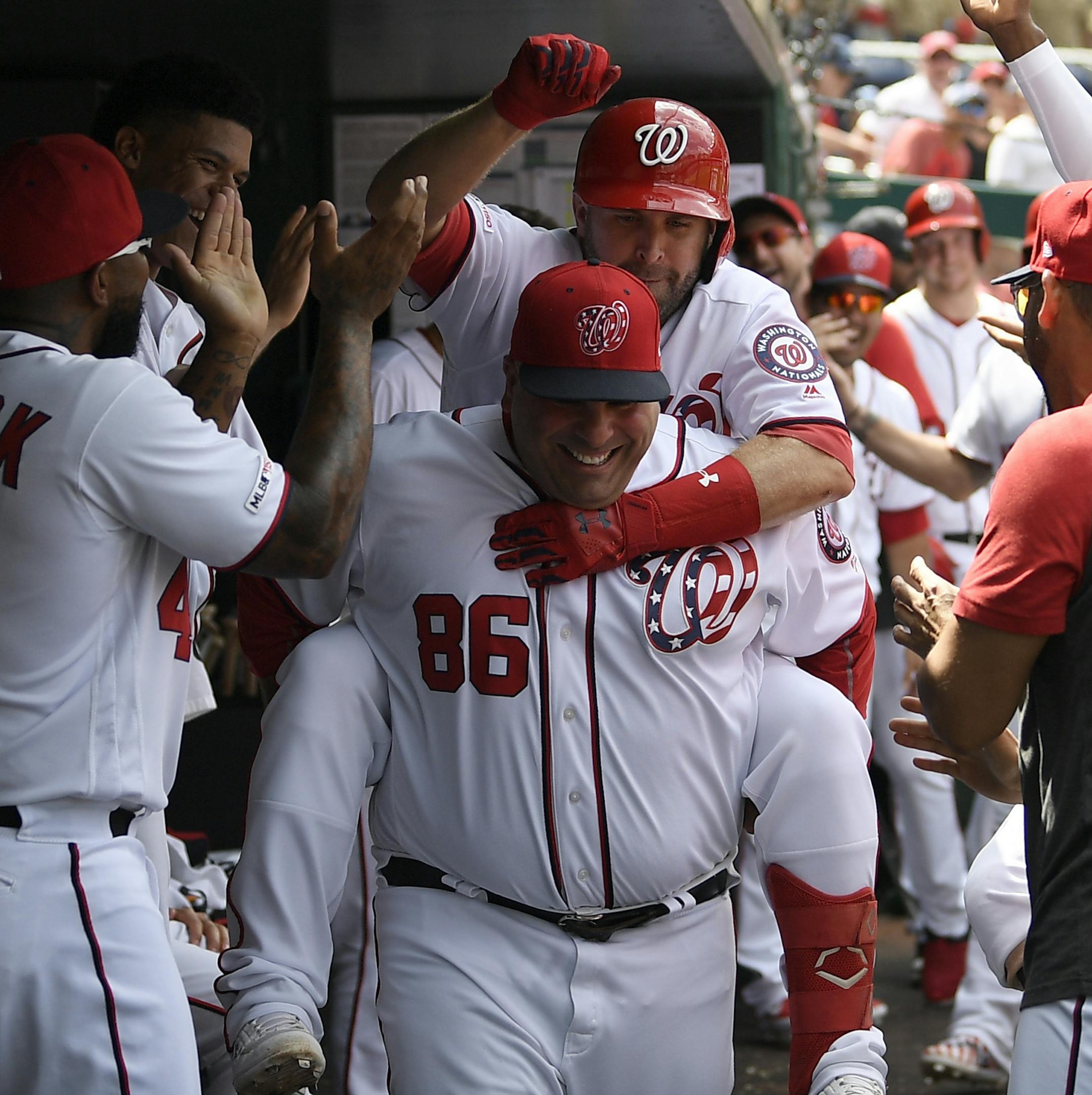 Washington Nationals' Brian Dozier, back, gets a ride from batting practice pitcher Ali Modami (86) in the dugout as he celebrates his three-run home run during the third inning of a baseball game against the Milwaukee Brewers, Sunday, Aug. 18, 2019, in Washington. (AP Photo/Nick Wass)