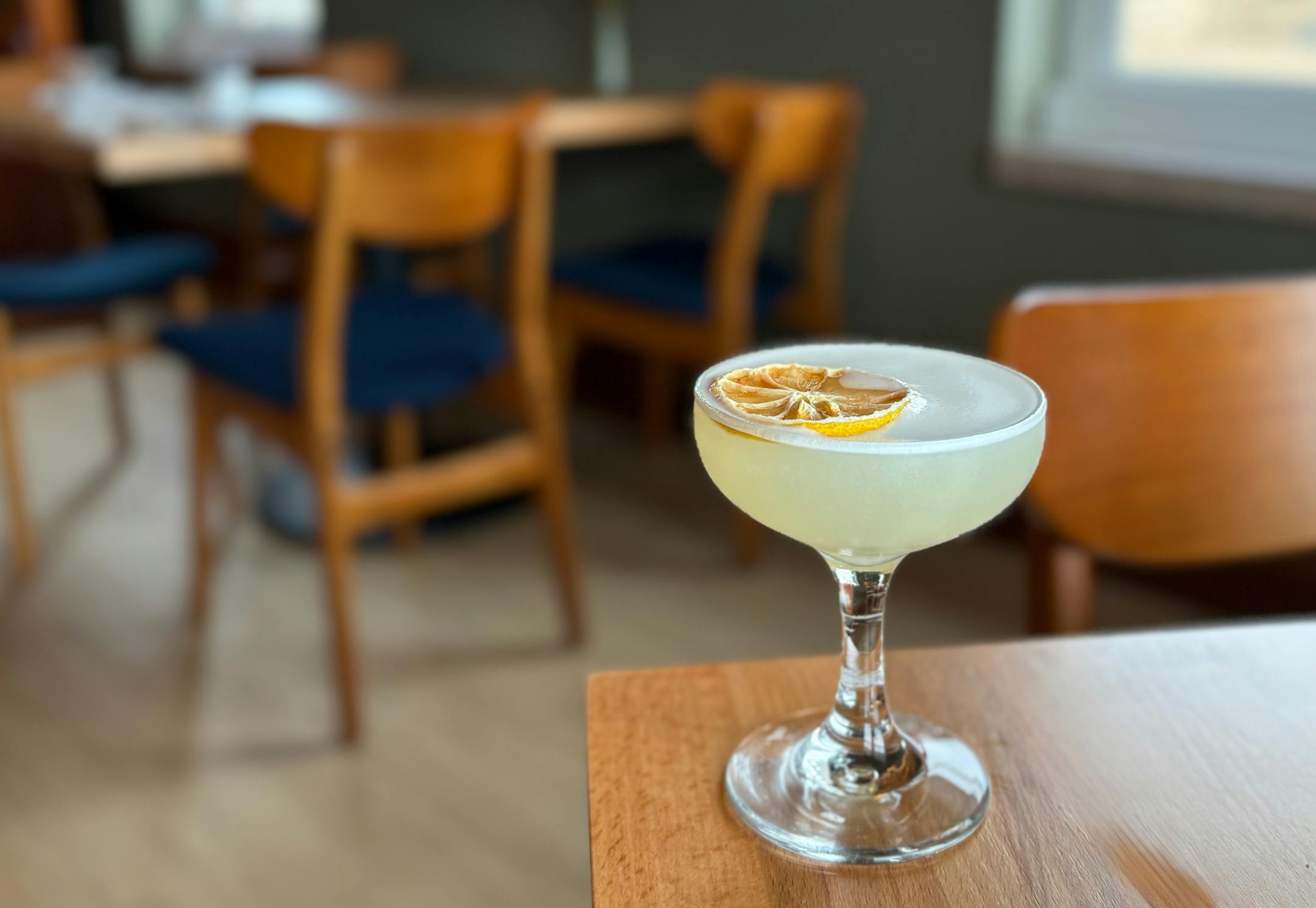 A light and frothy cocktail in a Nick and Nora glass, garnished with a dehydrated lemon.