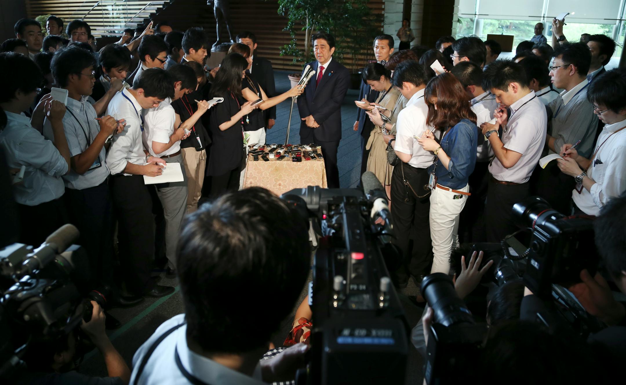 Japan's Prime Minister Shinzo Abe, rear center, speaks to reporters at his official residence in Tokyo, Friday, July 17, 2015. In a major reversal, Japan's leader announced Friday that the plans for the main stadium for the 2020 Olympics will be redone because of spiraling costs.