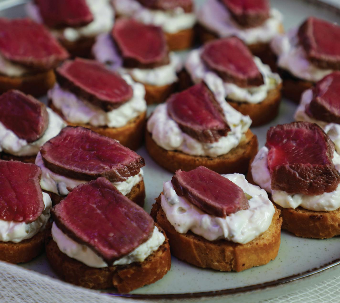 Seared Steak Slices on Sourdough Crisps with Artichoke-Jalapeño Spread is inspired by "Poltergeist" (1982). From "The Horror Movie Night Cookbook" (Ulysses, 2023).