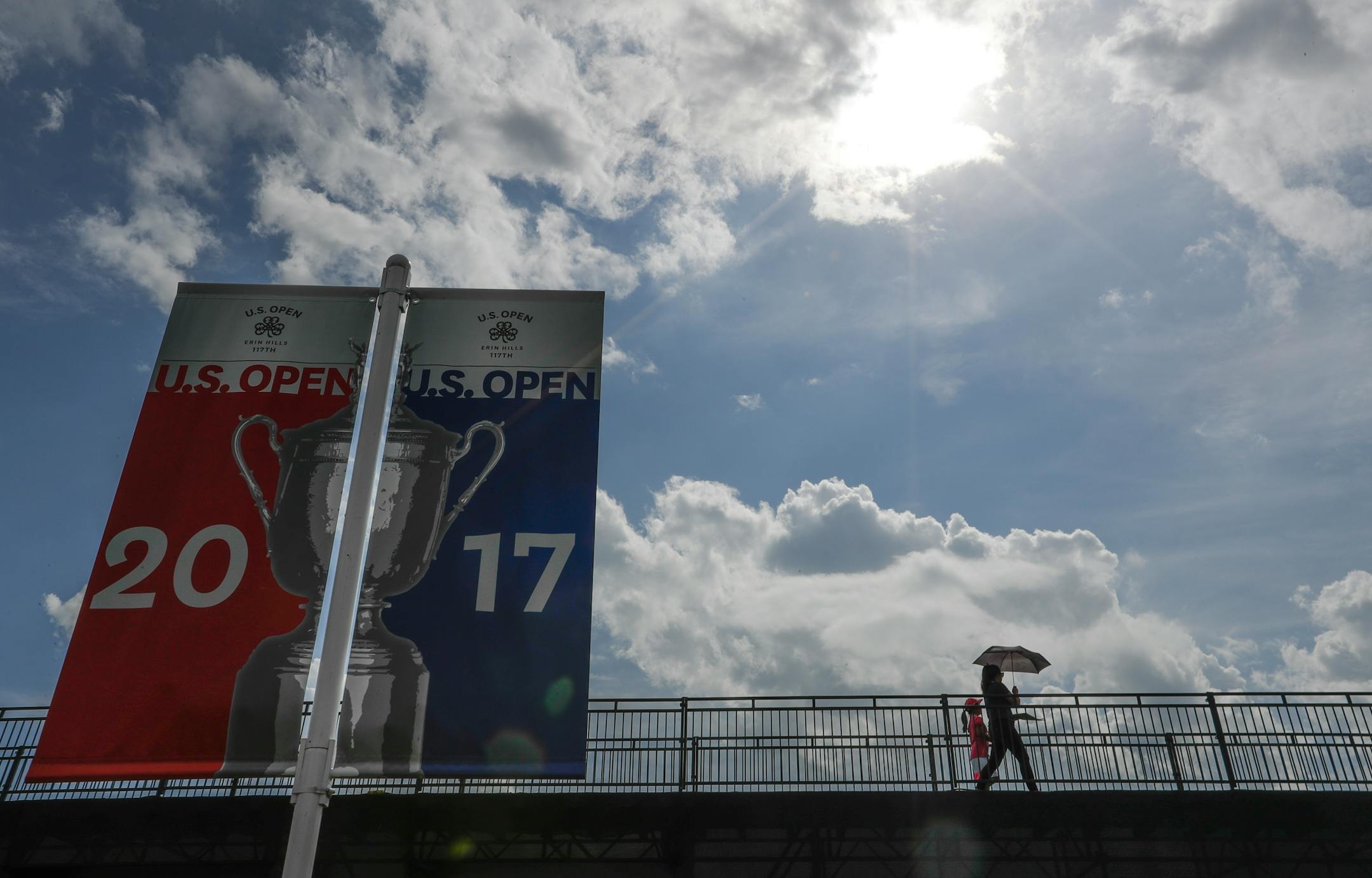 Fans walk on a bridges with an umbrella during a practice round for the U.S. Open golf tournament Wednesday, June 14, 2017, at Erin Hills in Erin, Wis. (AP Photo/Morry Gash)