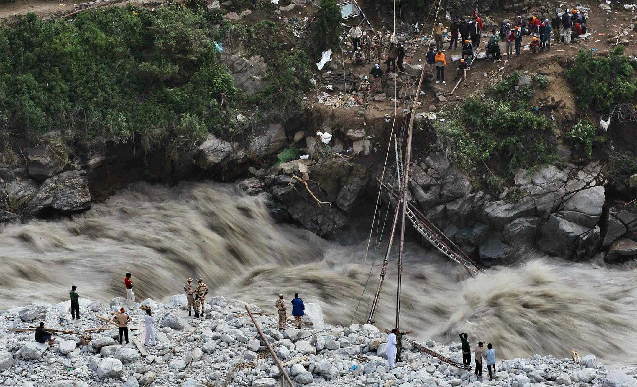 Water gushes down a river as Indian paramilitary soldiers stand near a temporary bridge after it was damaged as stranded pilgrims wait to be evacuated on the other side in Govindghat, India, Saturday, June 22, 2013. Soldiers were working to evacuate tens of thousands of people still stranded Saturday in northern India where nearly 600 people have been killed in monsoon flooding and landslides.