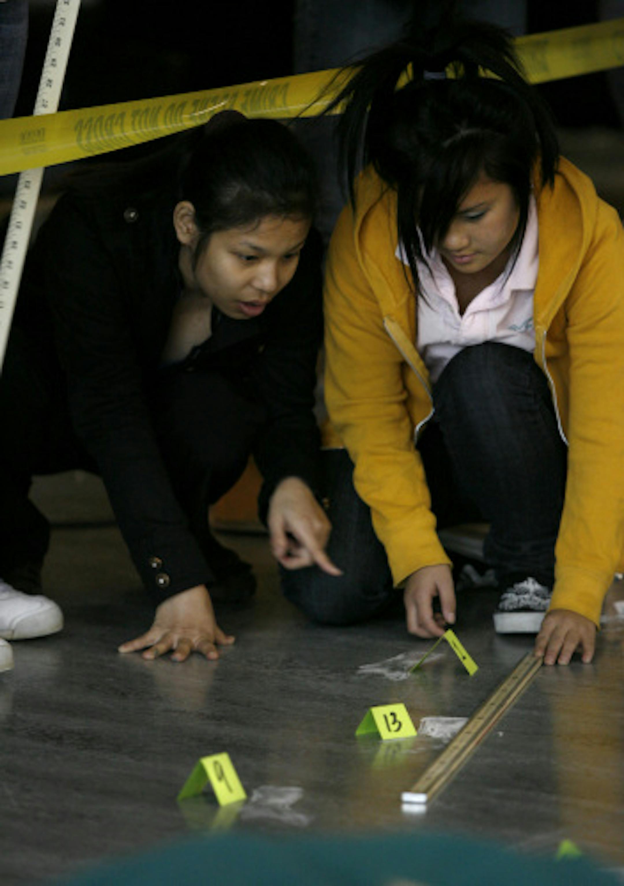 Paw Htoo , left, and Mai (Gina) Her measured footprints at a mock crime scene during their algebra class at Arlington High School. Students are now using science and math to investigate the crime, and every class is involved in solving the mystery.