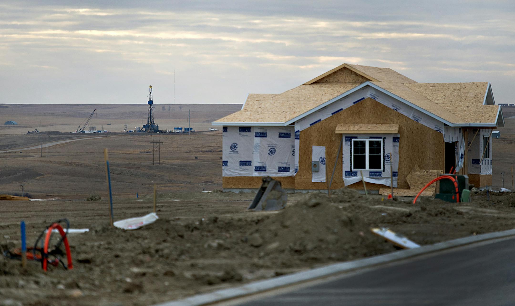 A crude oil drill rig stands in the distance of a single-family home under construction in Williston, North Dakota, U.S., on Monday, Feb. 13, 2012. The oil boom fueling the nation's lowest unemployment rate has put pressure on North Dakota's tight housing market. Officials expect some 1,200 apartments and single- family homes to be completed in Williston by summer. North Dakota will hold its Republican presidential caucus on March 6. Photographer: Daniel Acker/Bloomberg ORG XMIT: 140227233