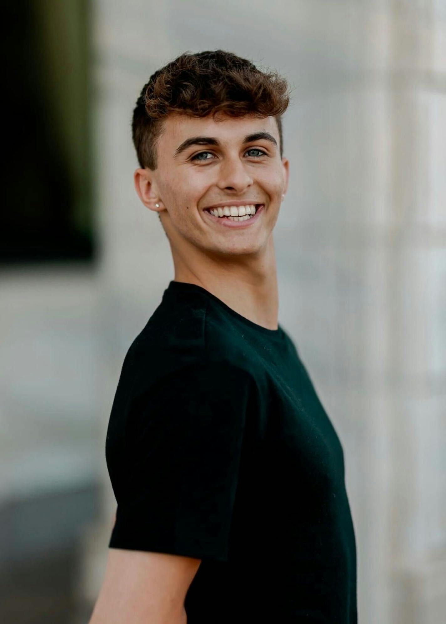 A slender man in his 20s wearing a fitted black T-shirt smiles at the camera