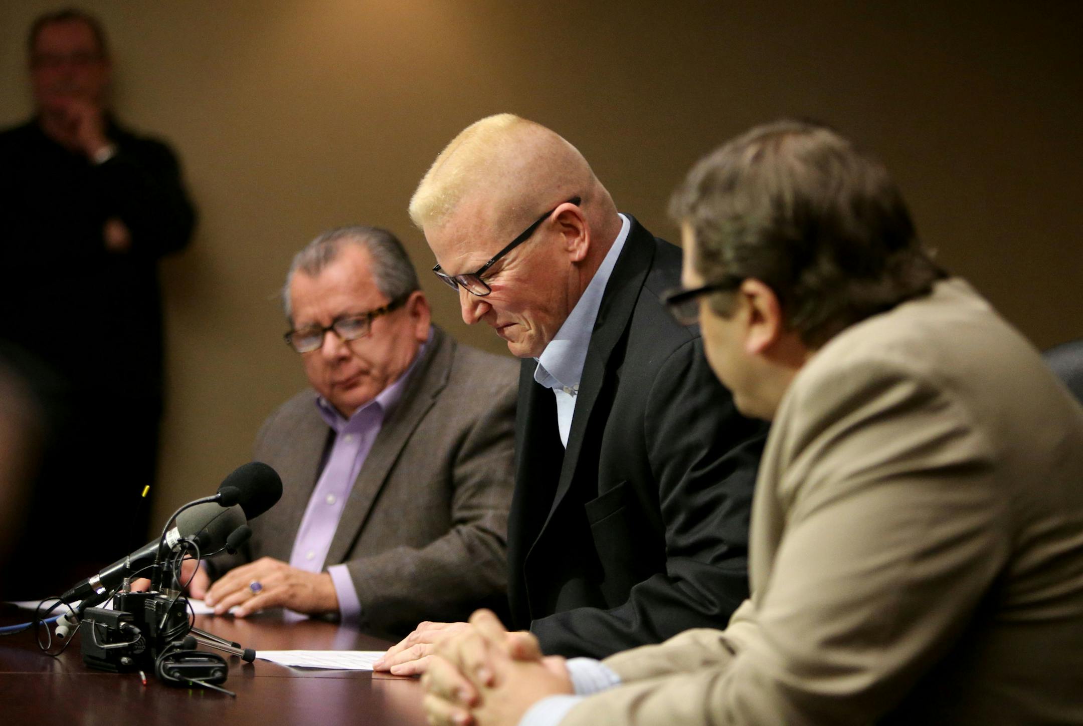 St. Paul Central High teacher John Eklbad, center, appears to grimace in pain while switching chairs before speaking to media members Tuesday, Dec. 22, 2015, at his attorneys' Bloomington MN, office. Ekblad recounted injuries and what he remembers of an assault by a student at St. Paul Central High on Dec. 6 that has left him with a head injury and constant headaches. He is flanked by his attorneys Philip Villaume, left, and Jeffrey Schiek, right.](DAVID JOLES/STARTRIBUNE)djoles@startribune.com