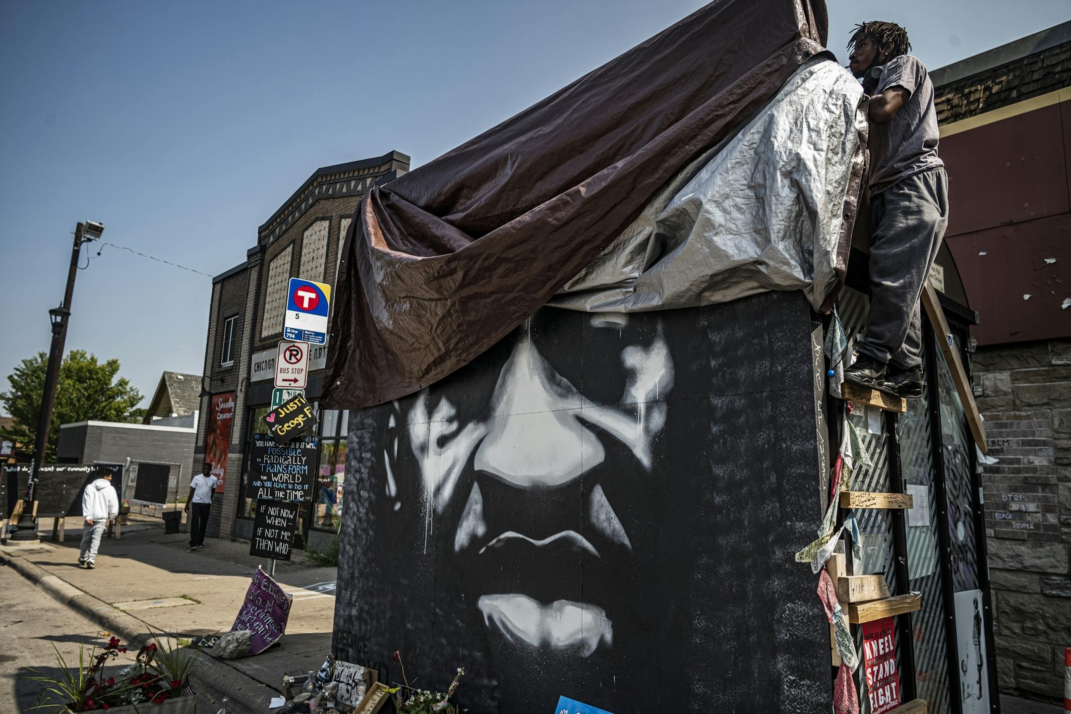 A portrait of George Floyd is unwrapped after the rain has cleared at the memorial site of 38th and Chicago Avenue.