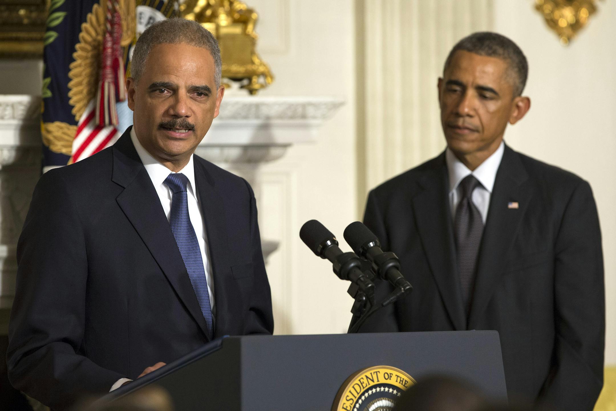 President Barack Obama, right, looks on as Attorney General Eric Holder speaks in the State Dining Room of the White House, on Thursday, Sept. 25, 2014, in Washington. Holder, who served as the public face of the Obama administration's legal fight against terrorism and weighed in on issues of racial fairness, is resigning after six years on the job. He is the first black U.S. attorney general. (AP Photo/Evan Vucci)