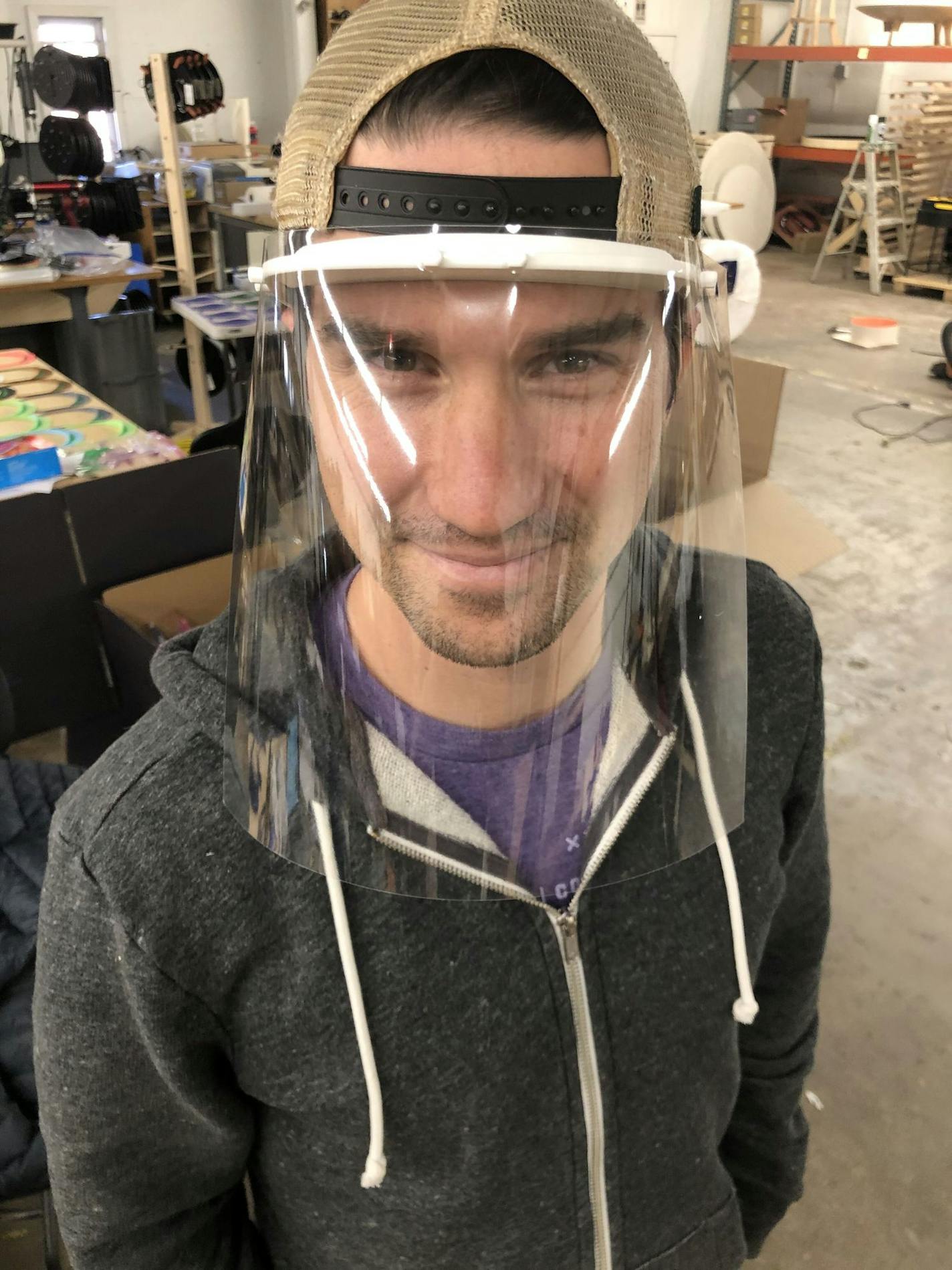 Tyler Cooper, co-owner of Nordeast Makers, models one of the thousands of protective face shields that volunteers are manufacturing and donating to healthcare workers around the state. Photo credit: Nordeast Makers