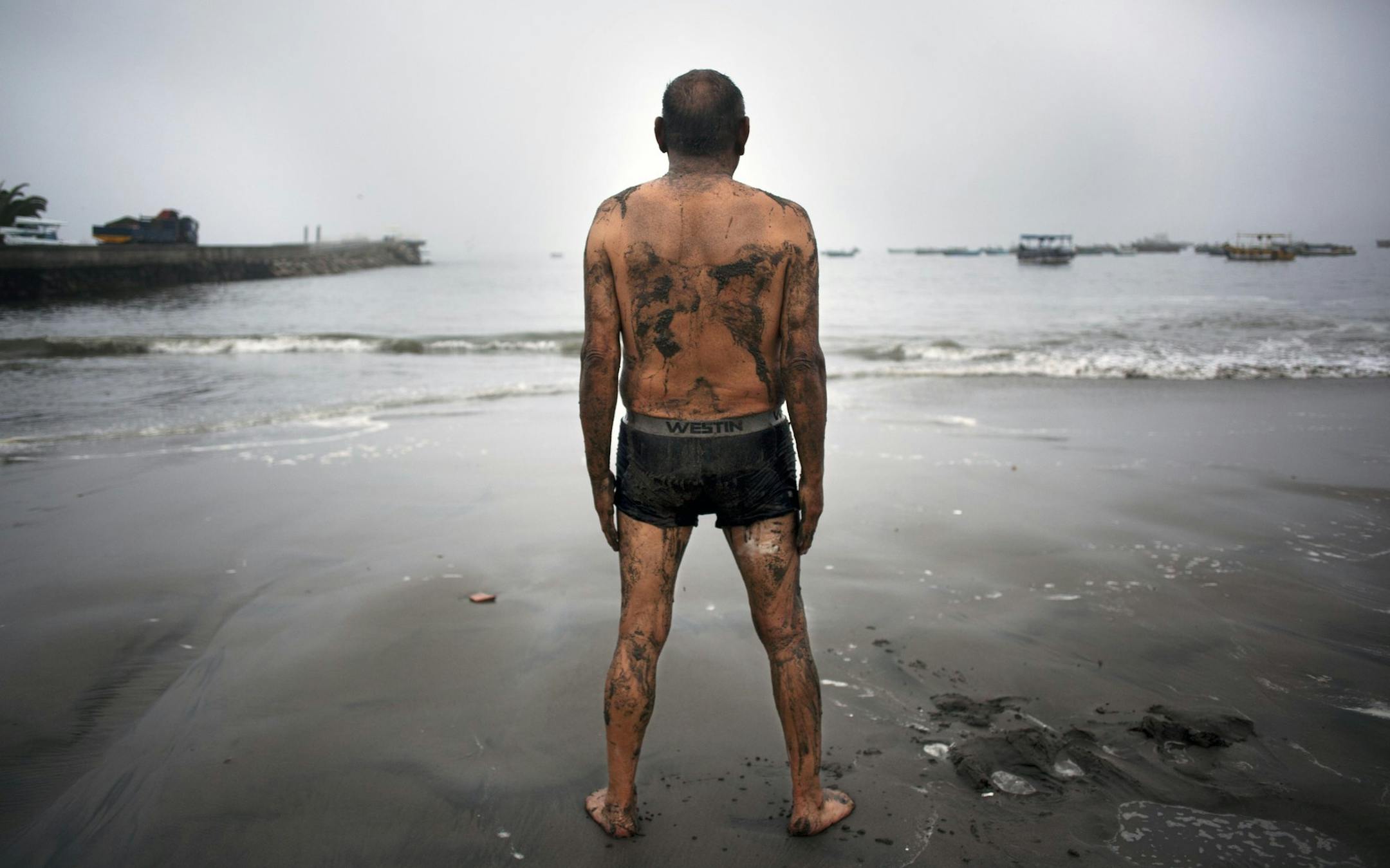Teodocio Perez, 71, covered with a thin layer of wet sand, looks out at the Pacific Ocean during his morning exercises on the Playa de Pescadores shore in Lima, Peru, Wednesday, April 2, 2014. Chilean authorities discovered surprisingly light damage Wednesday from a magnitude-8.2 quake that struck in the Pacific Ocean, Tuesday evening, near the mining port of Iquique, about 87 miles from the Peruvian border. Tsunami warnings issued for Chile, Peru and Ecuador have been lifted. Six deaths have be