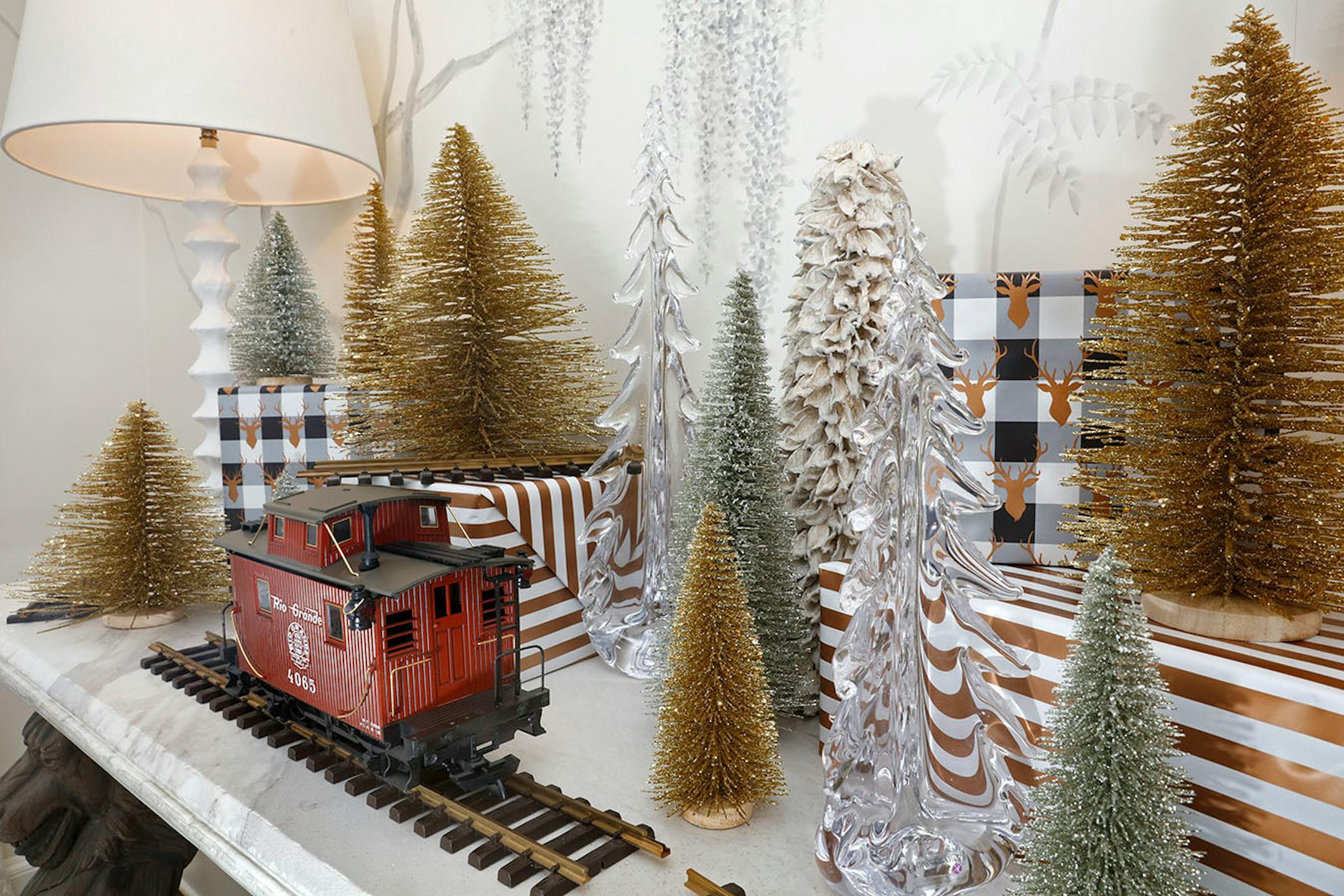 Choose objects with common elements such as the tree-shape and sparkly texture. To create a variety of heights and dimension, place some trees on top of boxes wrapped in simple-patterned paper repeating the colors in the tree display.