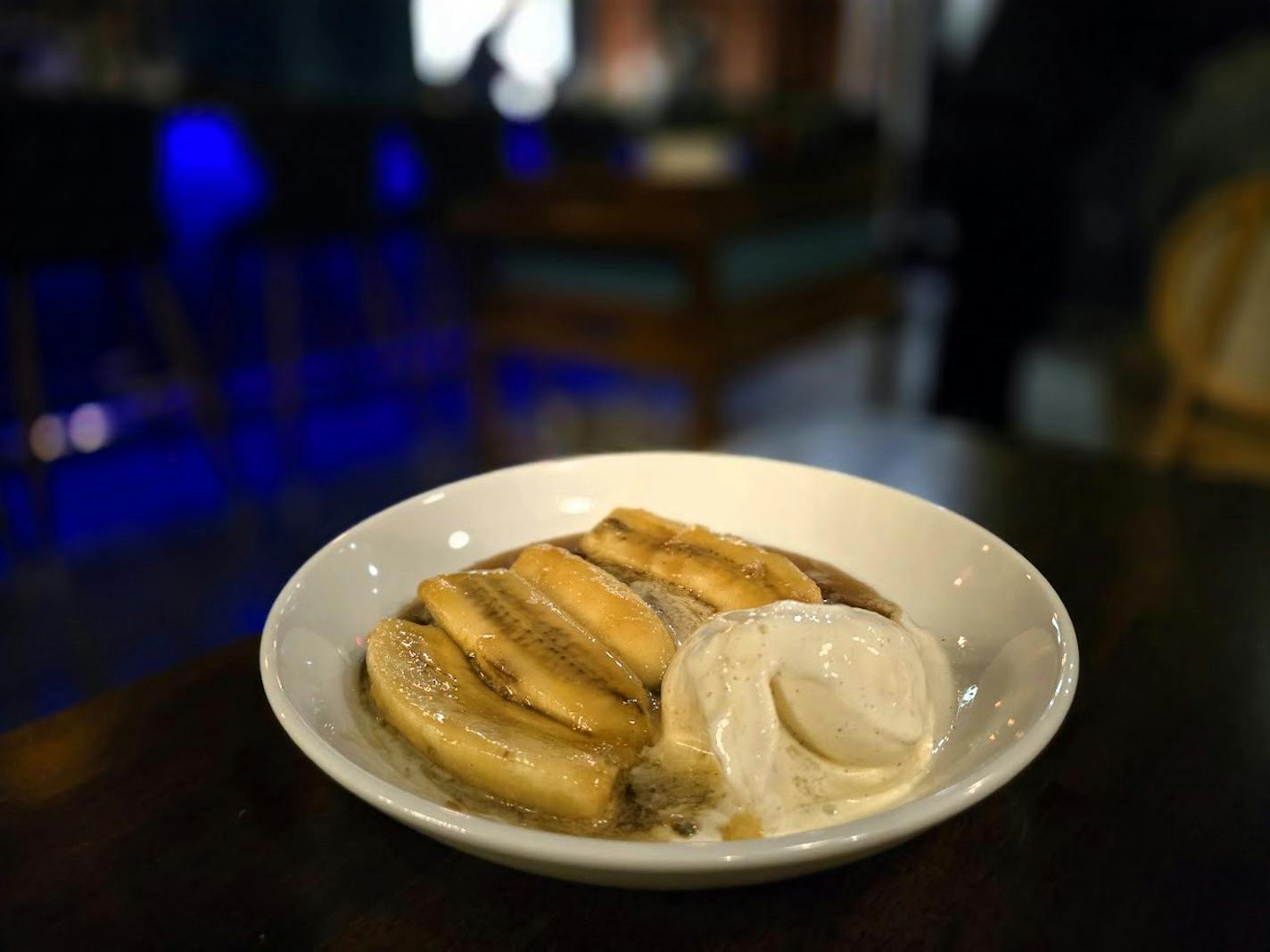 A white dish with slices of banana in a caramel sauce and a scoop of vanilla ice cream.