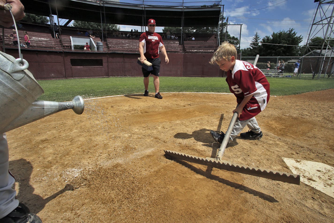 As water is sprinkled onto the dirt around home plate, Jace Griffin, 7, works a rake while his dad Ben Griffin looks on. Players and family members fill in as grounds crew to shape the field between games. ] A look at the Cold Spring Springers amateur baseball town team of Cold Spring. The teams have a tradition of family members playing and managing for many years with their children helping out as bat boys and grounds keepers. (MARLIN LEVISON/STARTRIBUNE(mlevison@startribune.com)