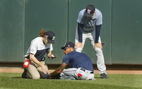 Byron Buxton, center, holds his ankle after he stumbled during an intrasquad game on Monday. He received attention from assistant athletic trainer Mat