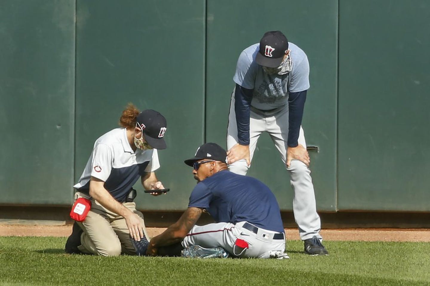 Byron Buxton, center, holds his ankle after he stumbled during an intrasquad game on Monday. He received attention from assistant athletic trainer Matt Biancuzzo, left, and manager Rocco Baldelli before he left the field on a cart.