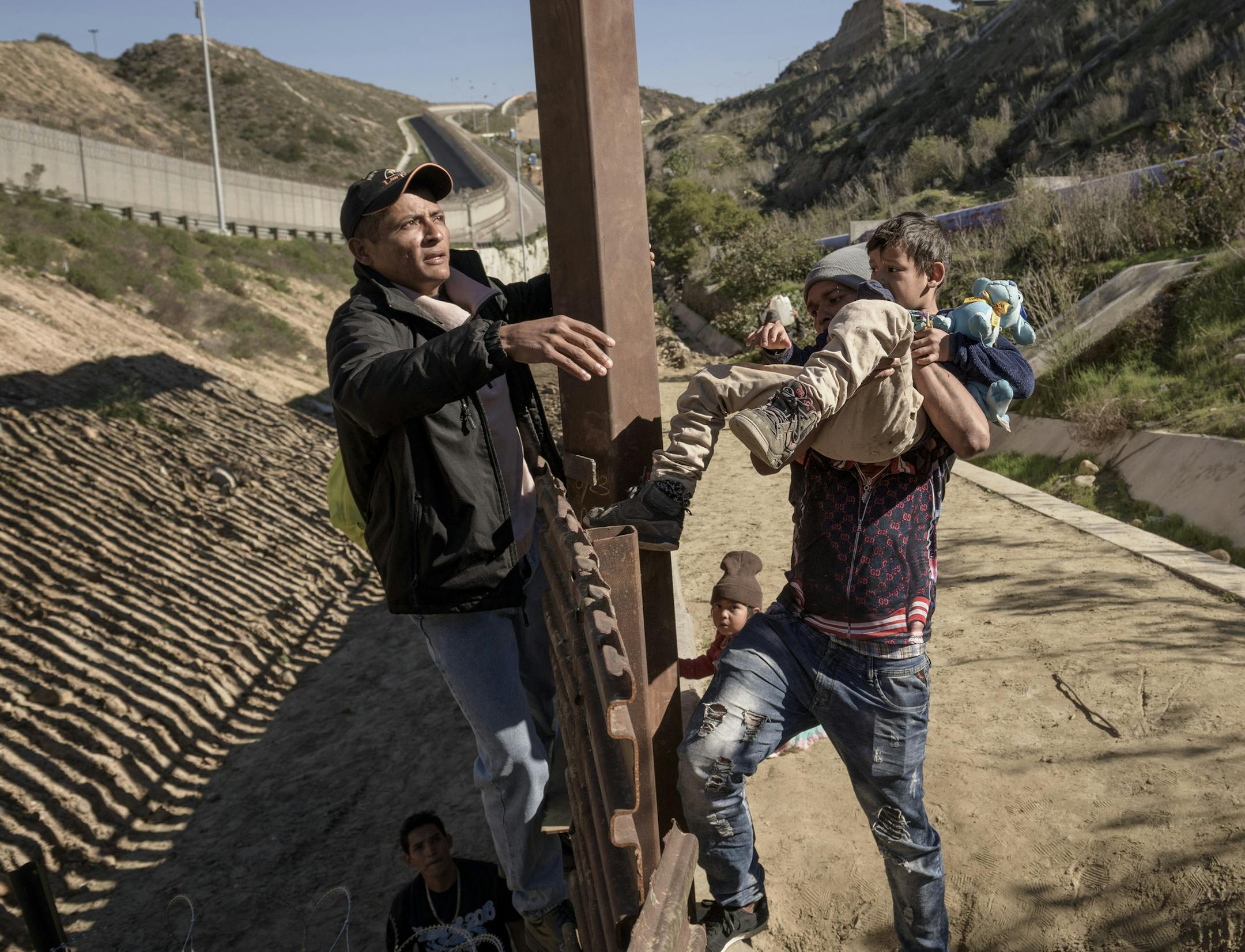 A man holds a Mexican migrant child as he jumps the border fence to get into the U.S. side to San Diego, Calif., from Tijuana, Mexico, Saturday, Dec. 29, 2018. Discouraged by the long wait to apply for asylum through official ports of entry, many migrants from recent caravans are choosing to cross the U.S. border wall and hand themselves in to border patrol agents. (AP Photo/Daniel Ochoa de Olza)