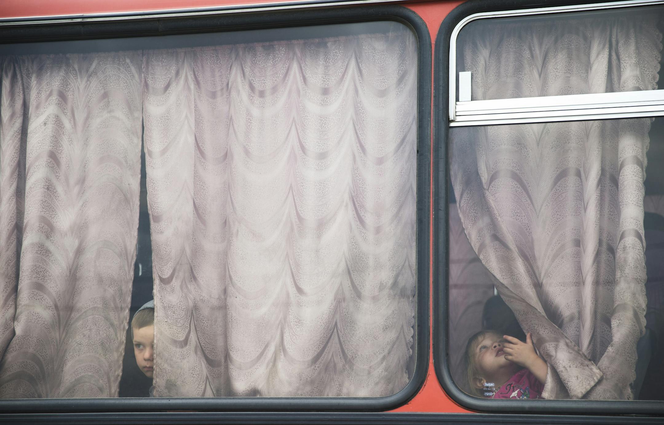 AP10ThingsToSee- Children look out from a bus before leaving for a train station at a refugee camp set up by the Russian Emergencies Ministry about 10 kilometers from the Russia-Ukrainian border, near Donetsk, Rostov-on-Don region, Russia, Monday, Aug. 18, 2014. (AP Photo/Pavel Golovkin) ORG XMIT: NC106