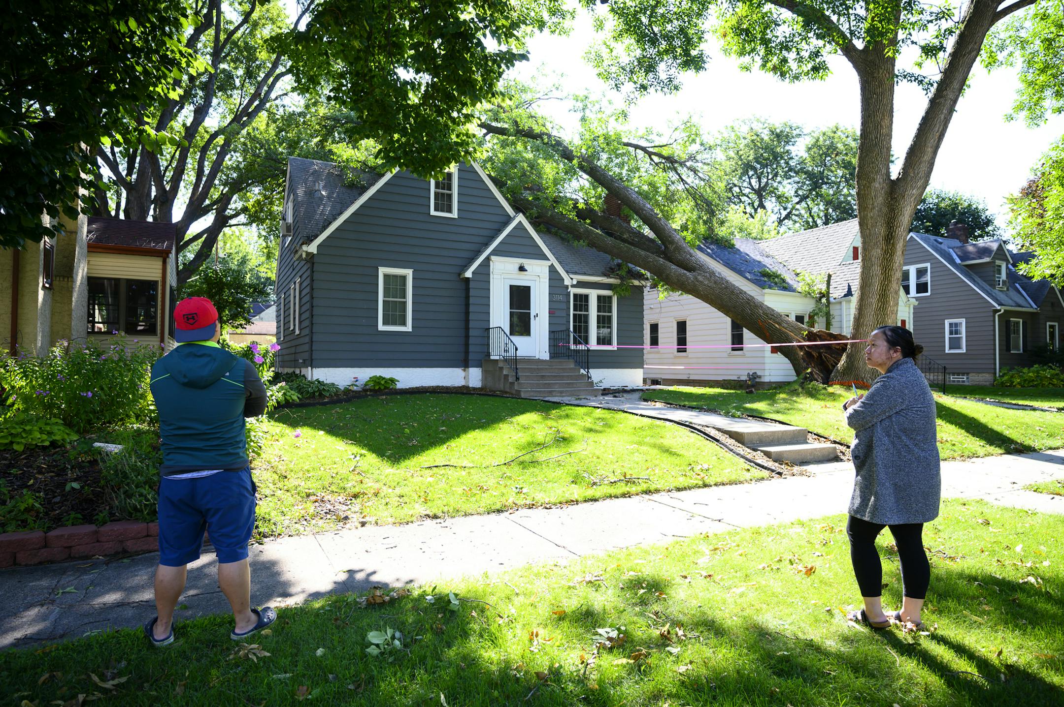 Lue Thao and Wendy Lor, of Robbinsdale looked over damage at their home Saturday, after a tree fell on the roof during Friday evening's storm.