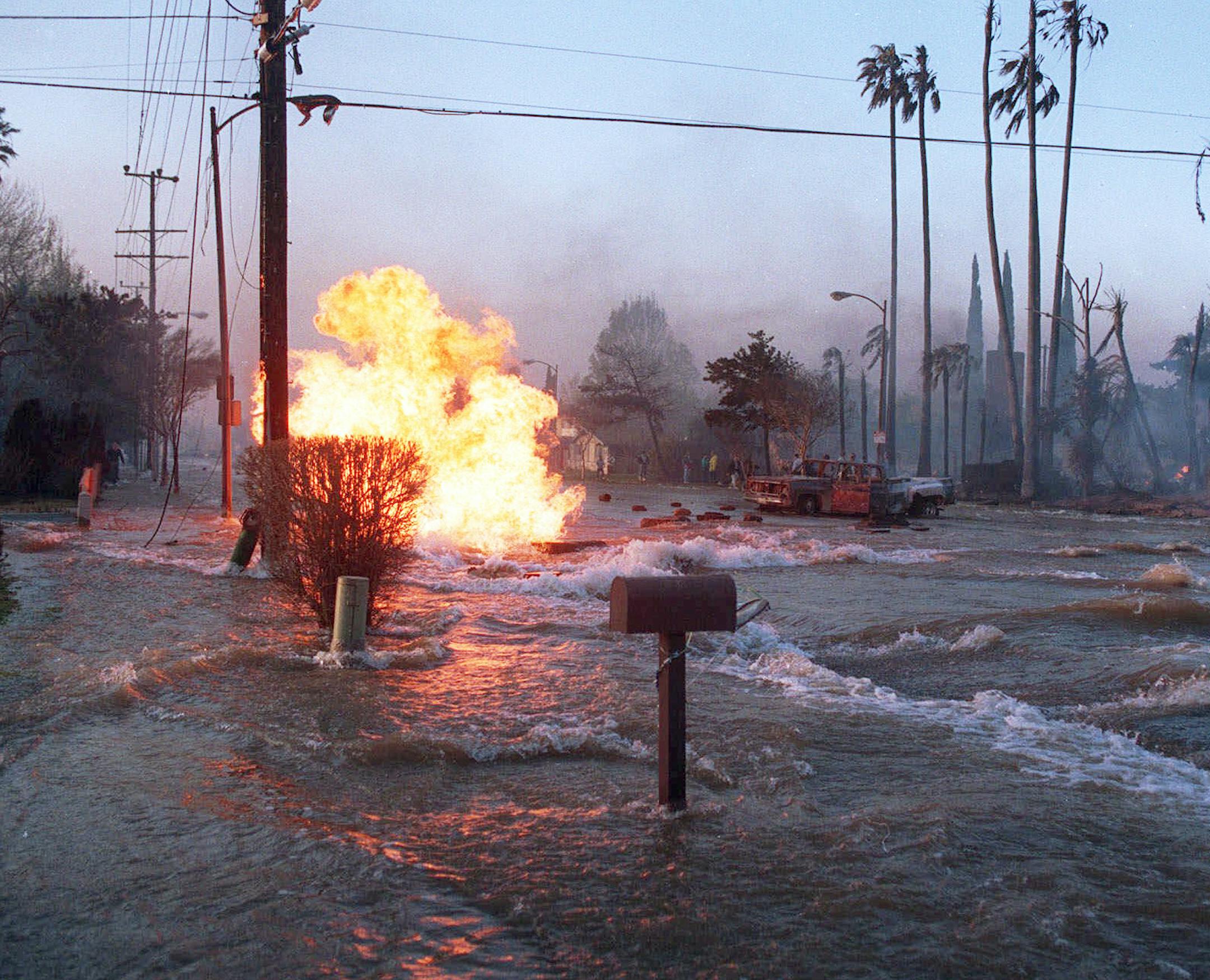 FILE - In this Jan. 17, 1994 file photo, gas from a ruptured supply line burns as water from broken water main floods Balboa Boulevard in the Granada Hills area of Los Angeles Monday morning, Jan. 17, 1994. The fire from the gas main destroyed two homes, right. The Northridge earthquake was felt over a broad area of Southern California, causing widespread death and destruction. ( AP Photo/Lenny Ignelzi, File)