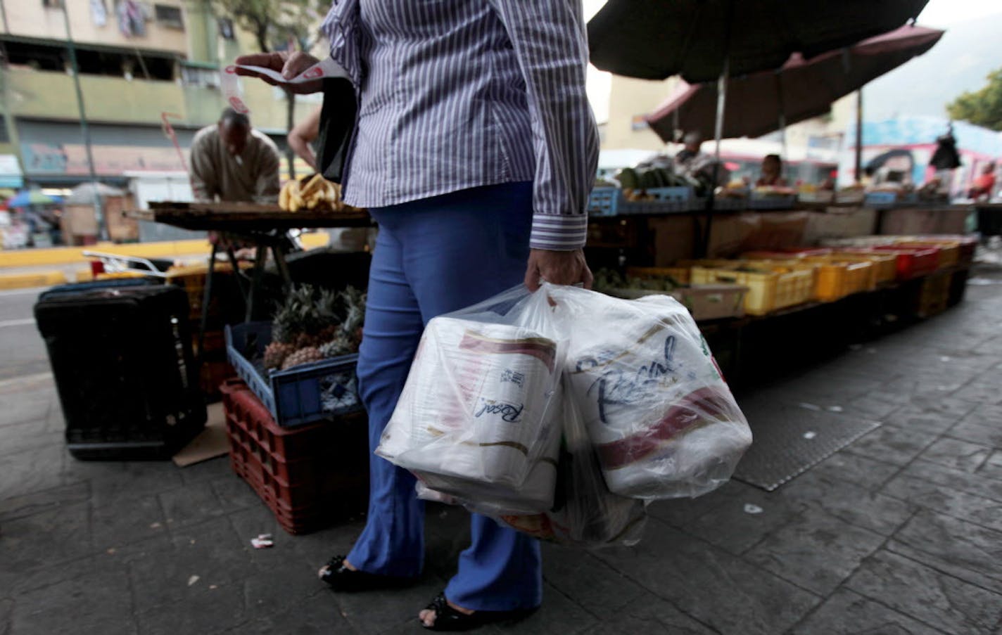 FILE- In this May 15, 2013 file photo, a woman who just bought toilet paper at a grocery store reads her receipt as she leaves the private store in Caracas, Venezuela. On Wednesday Sept. 10, 2014, Venezuela's President Nicolas Maduro reassured foreign creditors that his government will make good on a $4.5 billion foreign debt payment due next month. (AP Photo/Fernando Llano, File)