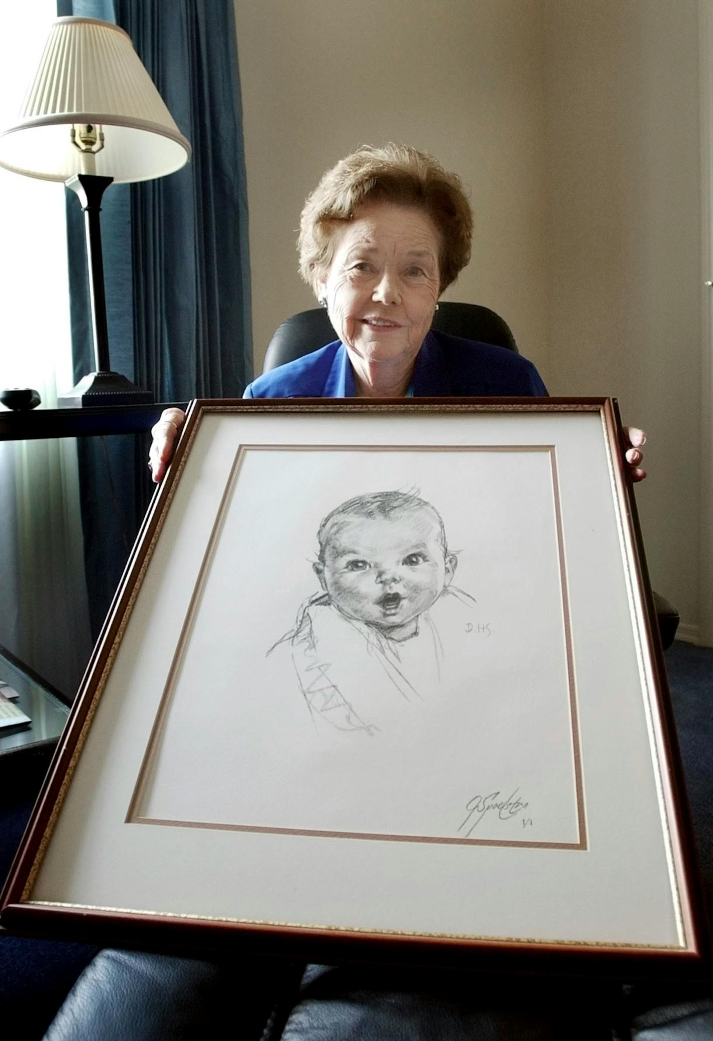 FILE - Ann Taylor Cook, poses at her Tampa, Fla., home Wednesday afternoon Feb. 4, 2004, with a copy of her photo that is used on all Gerber baby food products. Ann Turner Cook, whose cherubic baby face was known the world over as the original Gerber baby, has died. She was 95. Gerber announced Cook's passing in an Instagram post on Friday, June 3, 2022. (AP Photo/Chris O'Meara, File)