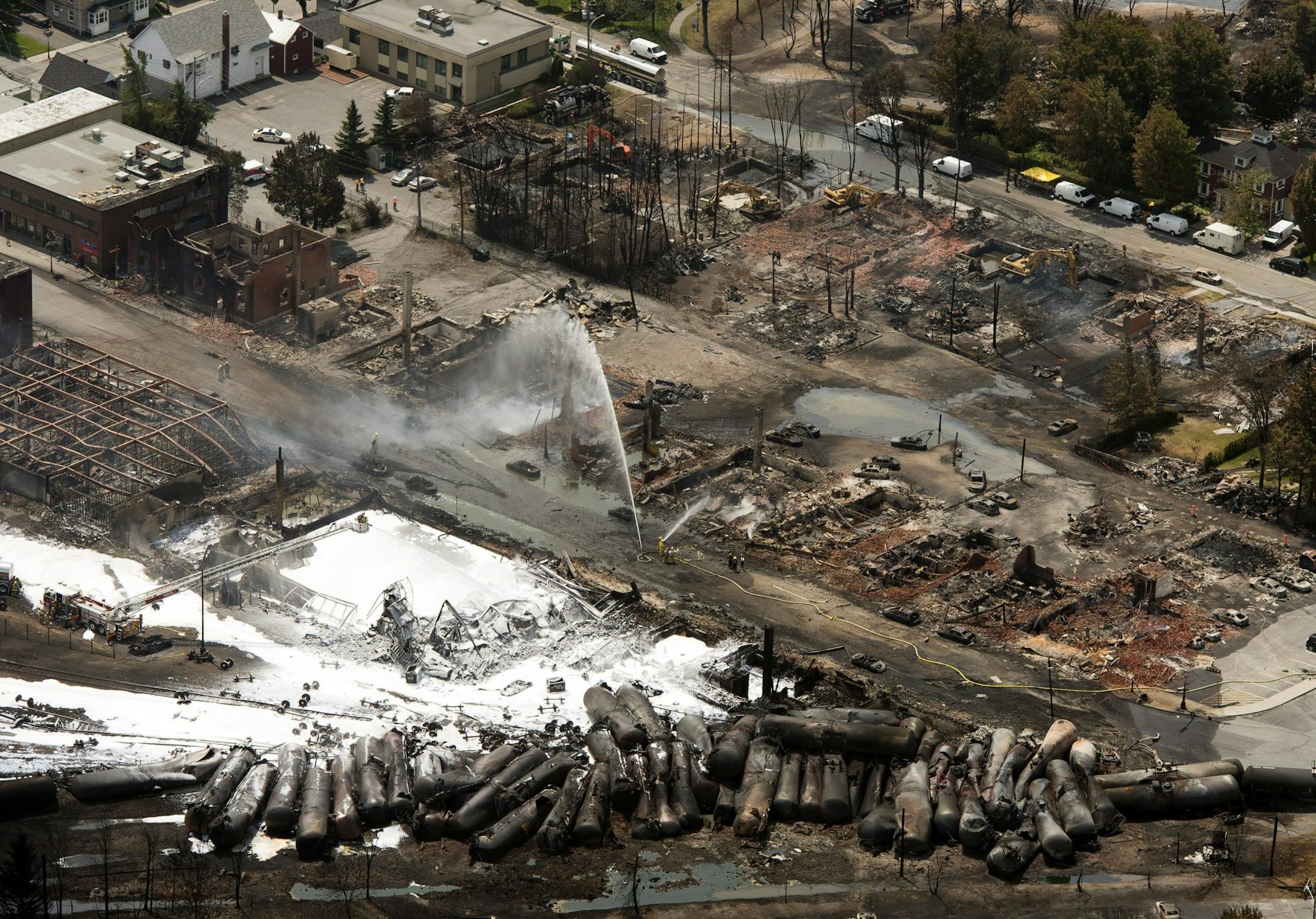 The downtown core lays in ruins as fire fighters continue to water smoldering rubble Sunday, July 7, 2013, in Lac Megantic, Quebec, after a train derailed ignited tanker cars carrying crude oil. The runaway train derailed, causing explosions and fires that destroyed the downtown district.