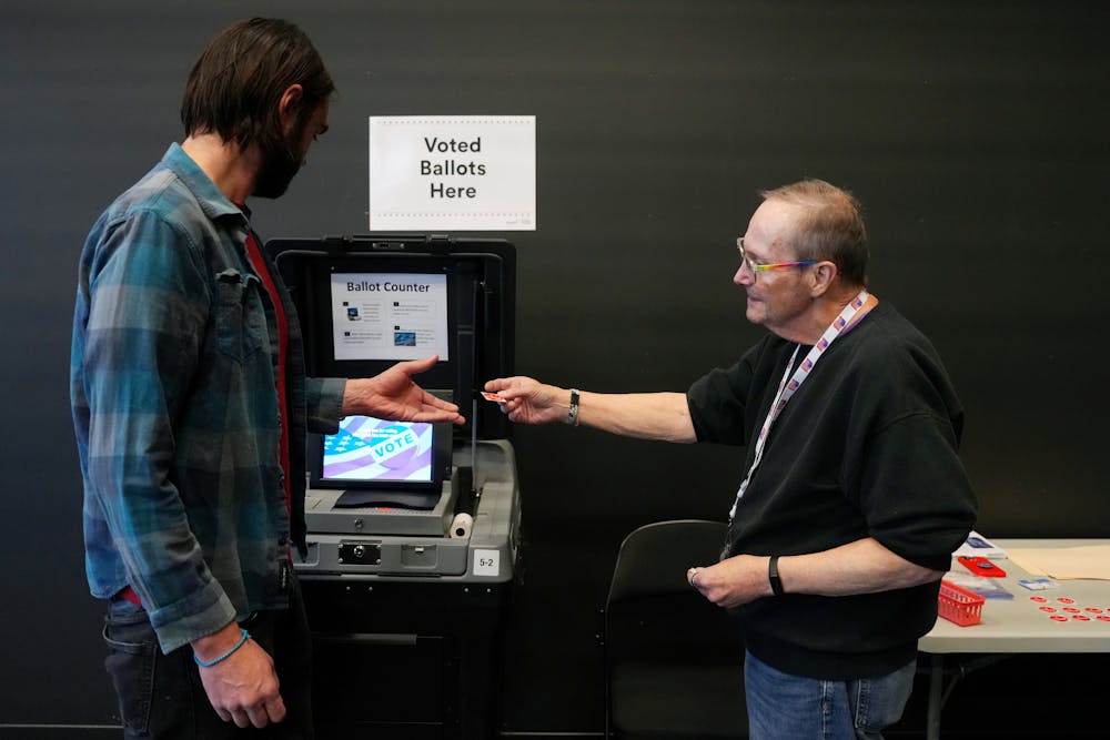 Election judge Rick Simon hands an “I Voted” sticker to Nokola Govich after he submitted his ballot on Election Day at the Capri Theater in Minneapolist.