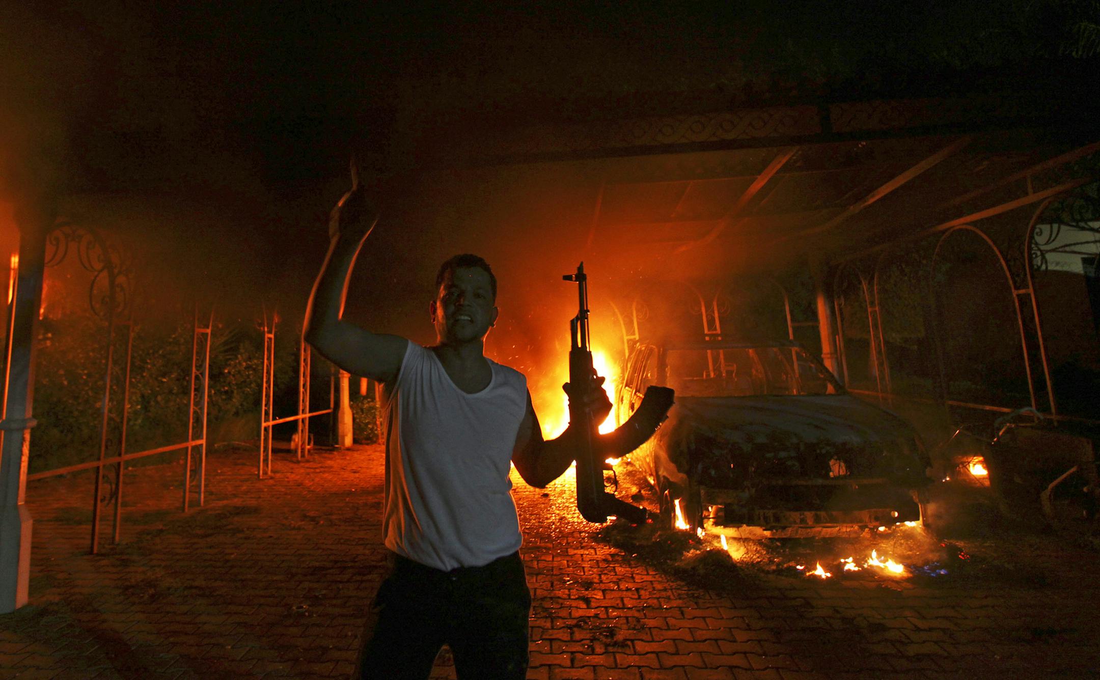 A protester reacts as the U.S. Consulate in Benghazi is seen in flames during a protest by an armed group said to have been protesting a film being produced in the United States September 11, 2012. An American staff member of the U.S. consulate in the eastern Libyan city of Benghazi has died following fierce clashes at the compound, Libyan security sources said on Wednesday. Armed gunmen attacked the compound on Tuesday evening, clashing with Libyan security forces before the latter withdrew as