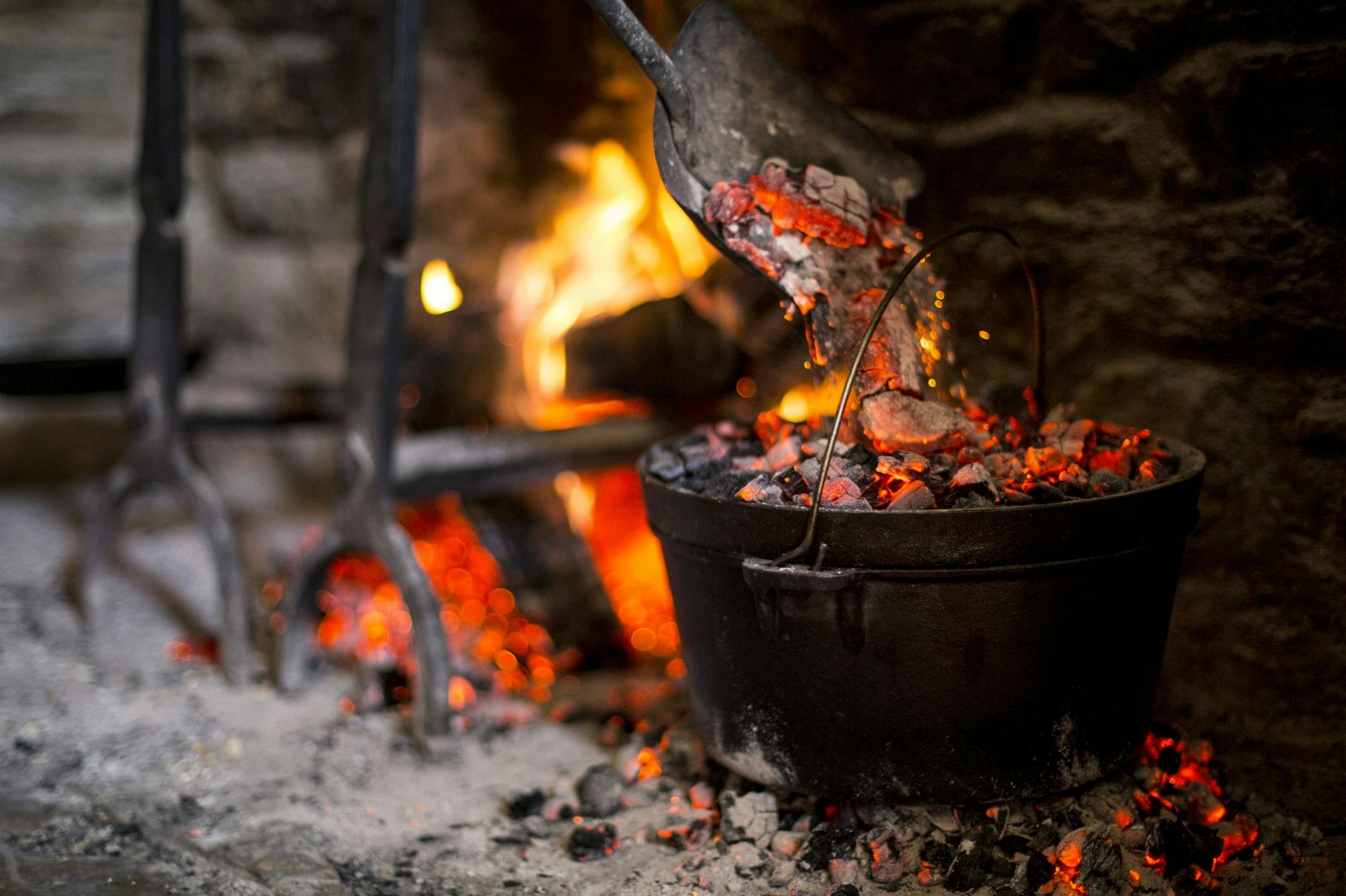 Missy McDonald pours hot coals on top of the kettle holding the spiced chicken and cabbage.