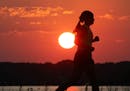 A runner makes her way along the shores of Lac La Belle in Oconomowoc, Wis., as the sun hangs low in the sky Tuesday, Aug. 2, 2016. (John Hart/Wiscons