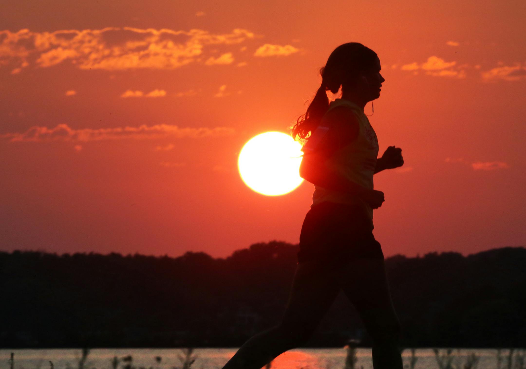 A runner makes her way along the shores of Lac La Belle in Oconomowoc, Wis., as the sun hangs low in the sky Tuesday, Aug. 2, 2016. (John Hart/Wisconsin State Journal via AP)