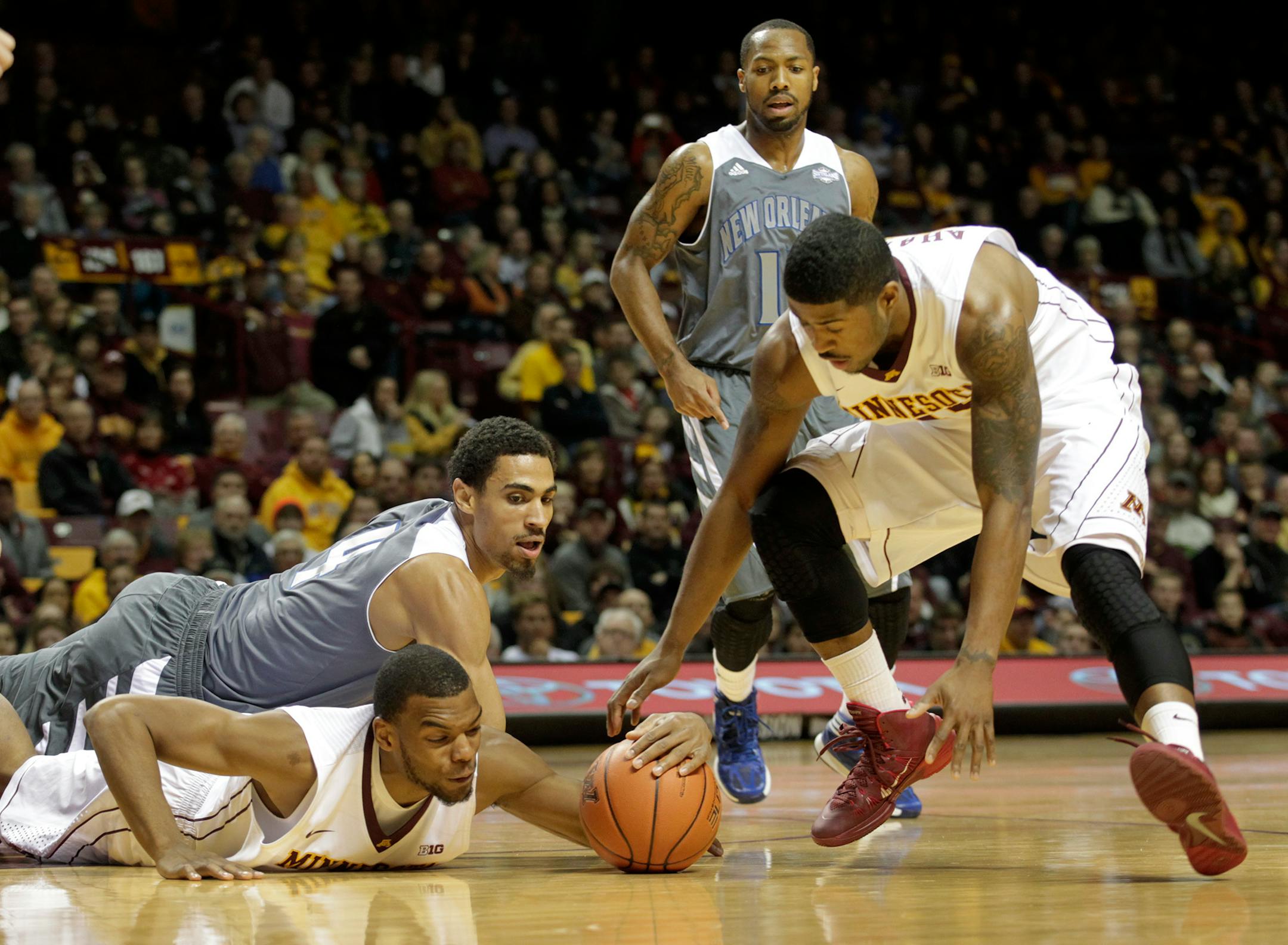 Minnesota's Andre Hollins, bottom, tries to control the loose ball with teammate Maverick Ahanmisi, right, against New Orleans forward Cory Dixon (4) during the first half of an NCAA college basketball game, Saturday, Dec. 7, 2013, in Minneapolis. New Orleans guard Isaac Mack (11) looks on during the play. Minnesota won 80-65. (AP Photo/Paul Battaglia)