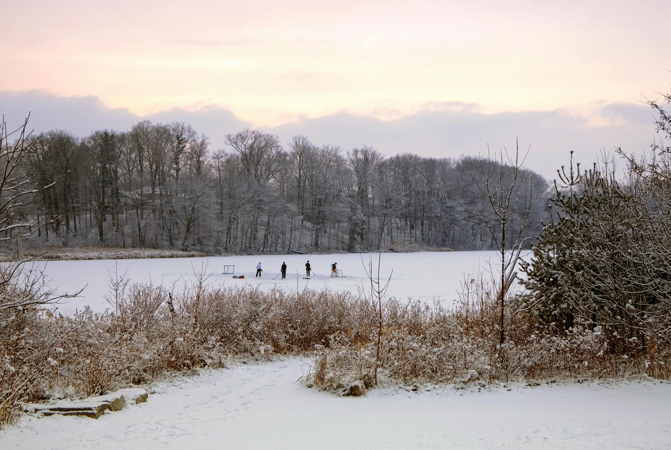 Young men practising ice hockey on frozen pond in a park at dusk