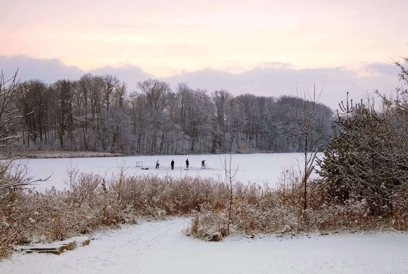 Young men practising ice hockey on frozen pond in a park at dusk