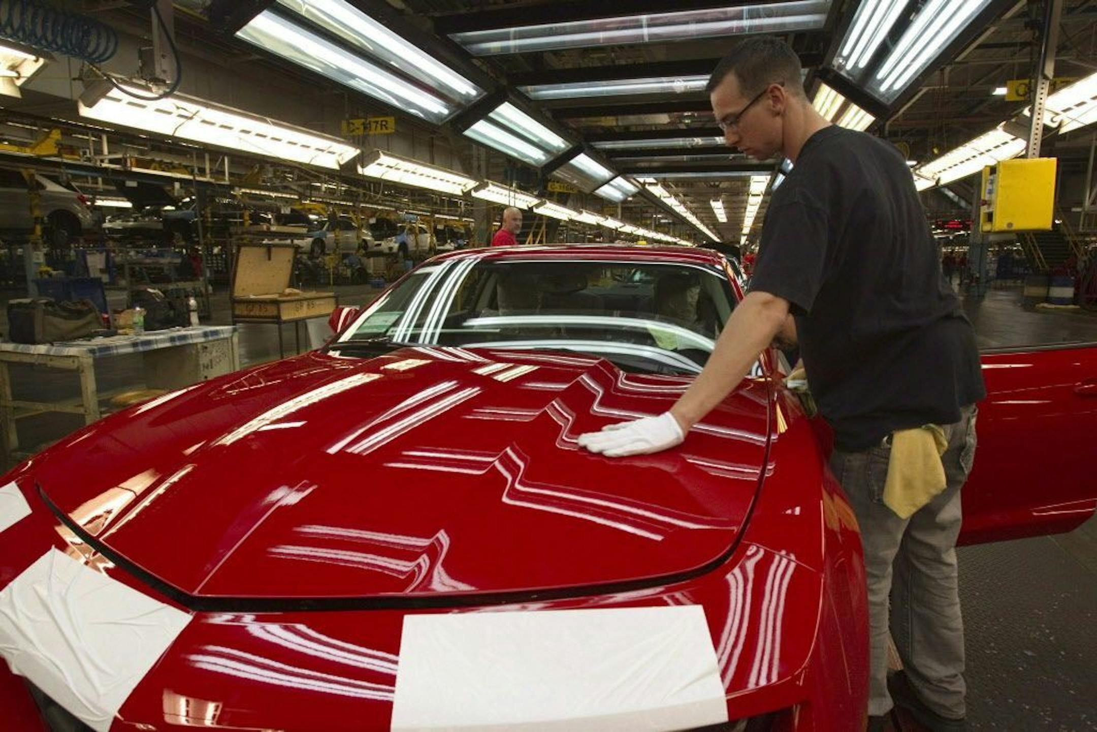 FILE - In this June 10, 2011, file photo, a worker checks the paint on a Camaro at the GM factory in Oshawa, Ontario. General Motors is closing a Canadian plant at the cost of about 2,500 jobs, part of a much broader, company-wide restructuring that will cut 14,700 jobs.