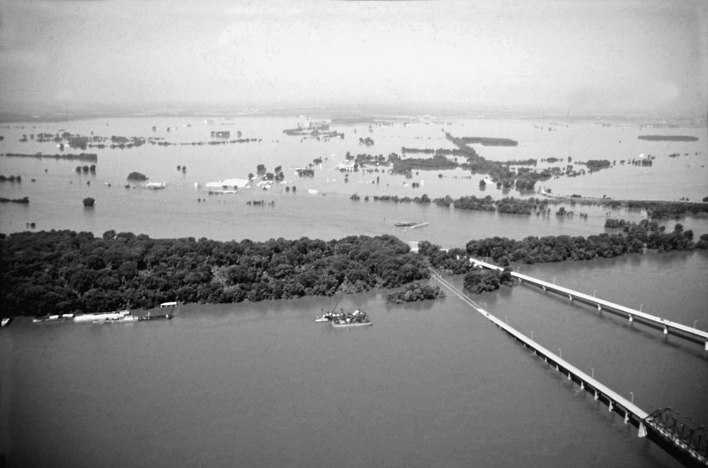 In July 1993, one day after the West Quincy levee break, 14,000 acres of land flooded. In the foreground, the Memorial Bridge had been underwater for over a week. Just north of that, the Bayview Bridge - the only means of crossing the Mississippi between St. Louis and Keokuk, Iowa - succumbed to the river.