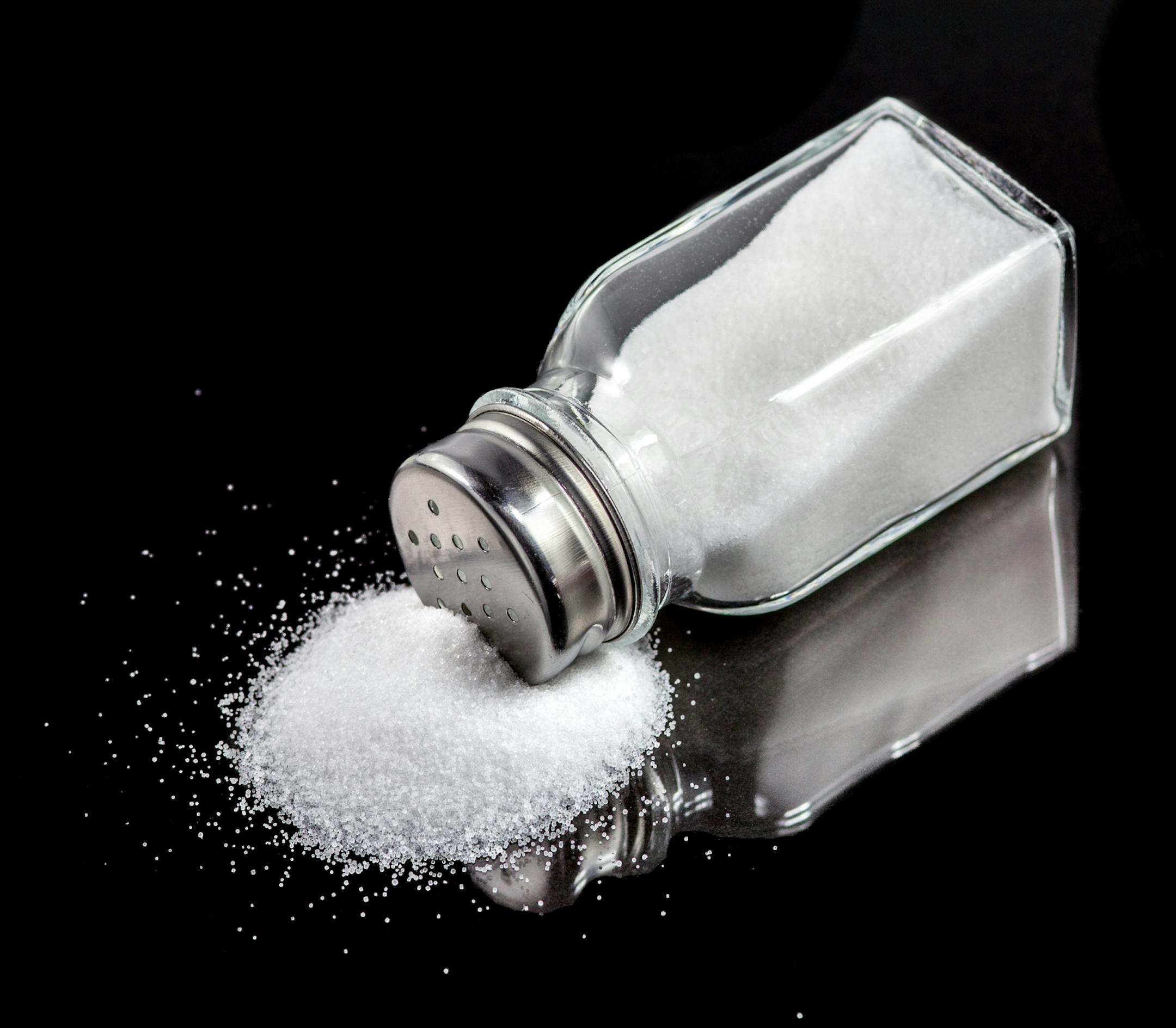 Salt shaker with spilled salt on a black background. istock