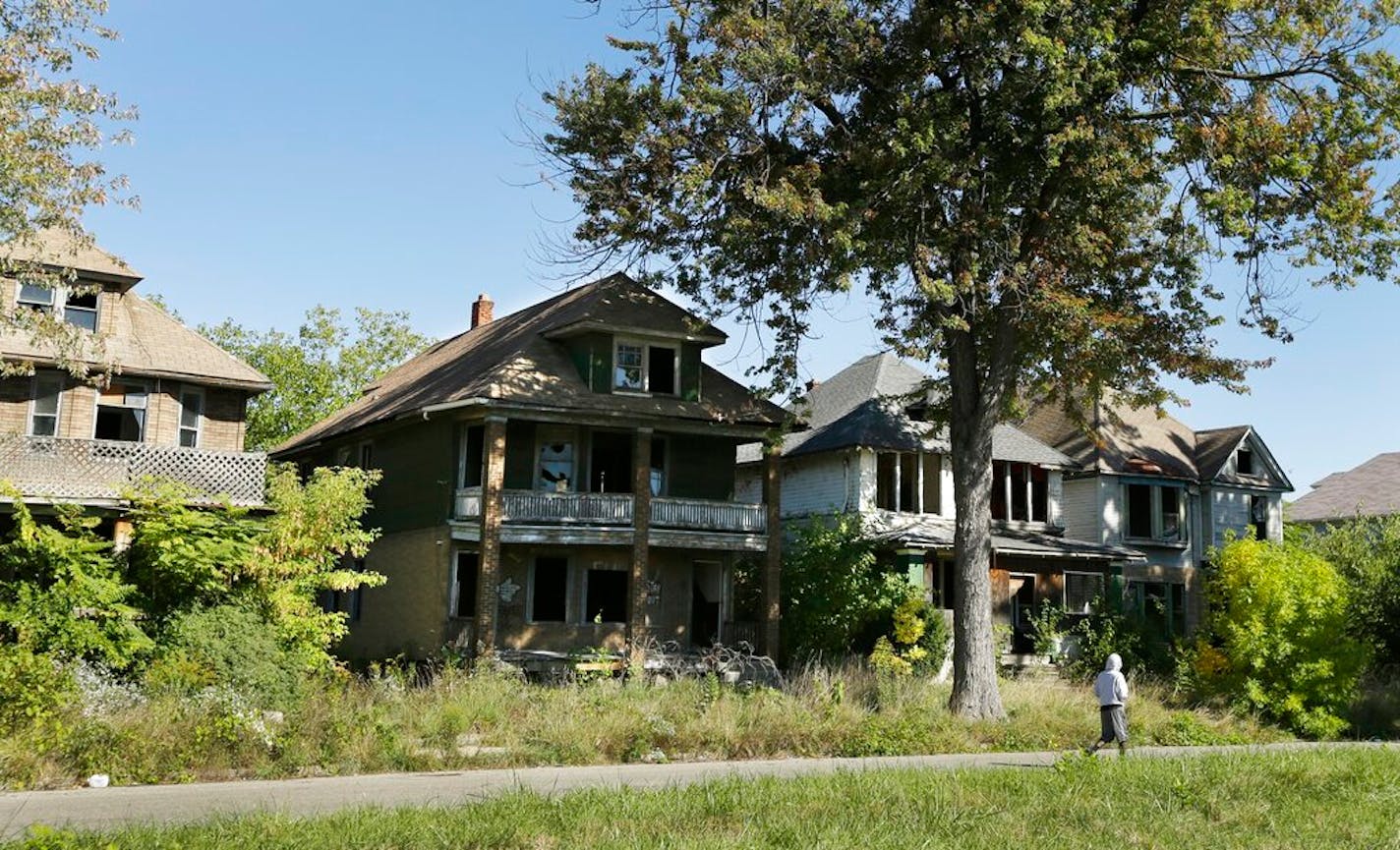 FILE - In this Sept. 26, 2013 file photo a young man walks in front of a row of abandoned houses in Detroit. Detroit has thousands of decrepit and abandoned homes and buildings. The city's proposal to emerge from bankruptcy includes a plan to demolish them. (AP Photo/Carlos Osorio, File)