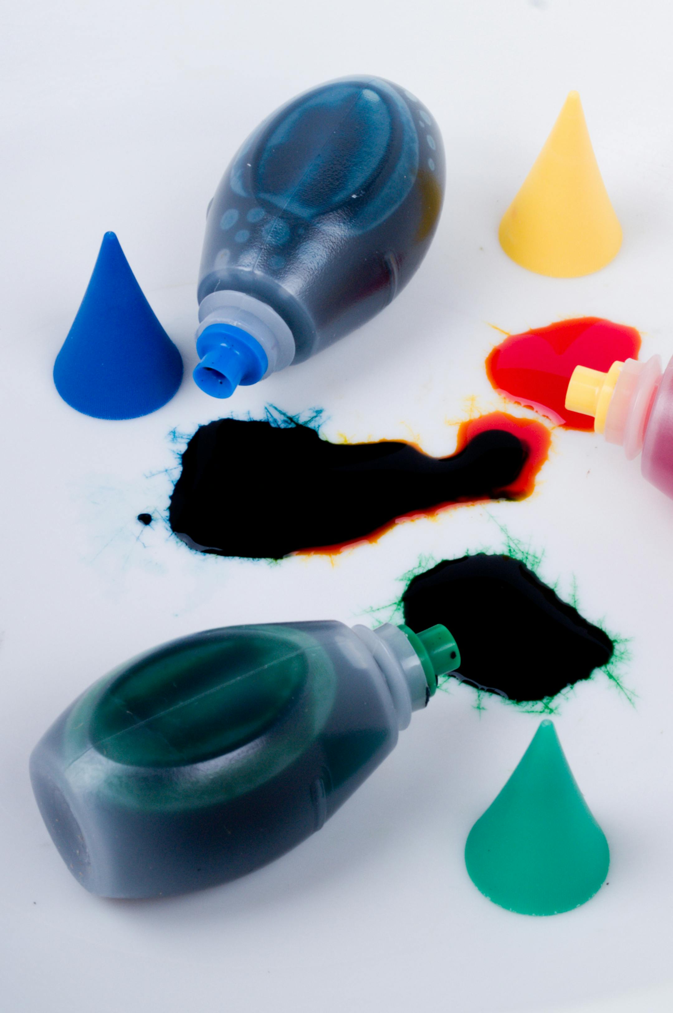 Blue, green, and yellow bottles of dye lay spilled among colored puddles.