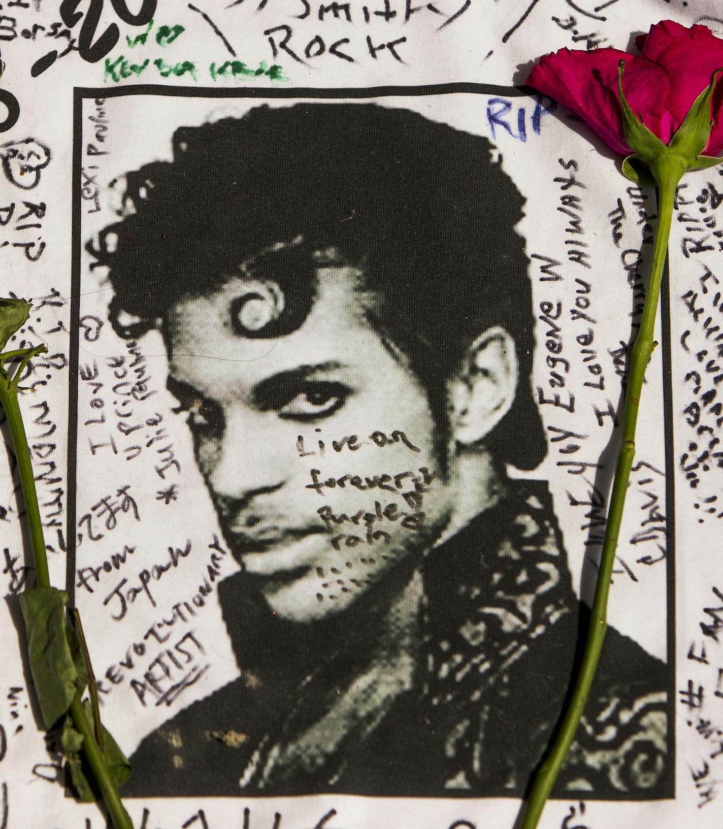 Flowers lay on a T-shirt signed by fans of singer Prince at a makeshift memorial place created outside Apollo Theatre in New York, Friday, April 22, 2016. The pop star died Thursday at the age of 57. (AP Photo/Andres Kudacki)