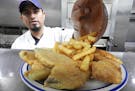 Cook Alvaro Aguilera adds french fries to a plate of fried fish at the 5 O&#x2019;ClockClub. On Fridays, the restaurant typically serves more than 500
