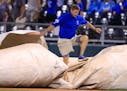 A grounds crew member works to cover the field during the fifth inning of a baseball game between the Kansas City Royals and the Minnesota Twins at Ka
