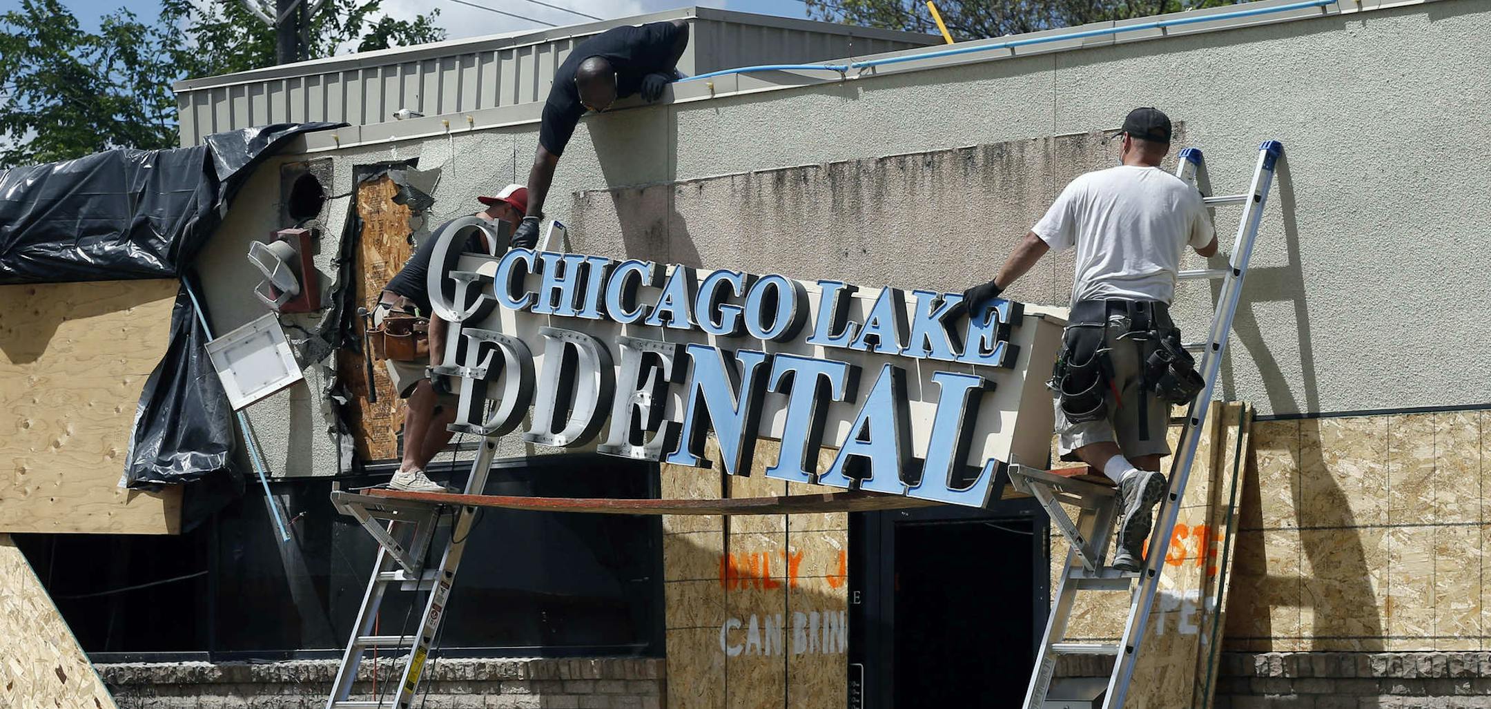 Workers remove the sign on June 23, 2020, at Ali Barbarawi's Chicago Lake Family Dental practice in Minneapolis, which was forced to close by the coronavirus pandemic, then destroyed in the unrest following the death of George Floyd at the hands of Minneapolis police. The destruction is a loss not just for him, but for his staff and patients, he said, and insurance will cover, at most, half of what he'll need to rebuild. (AP Photo/Jim Mone)