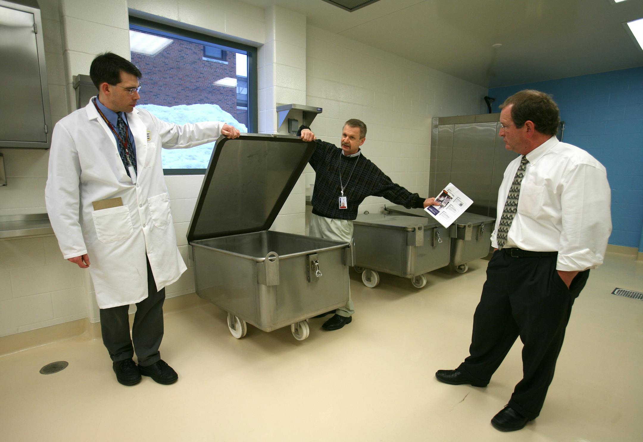 Ron Joki, center, explained the function of a stainless-steel bin in the new lab at the U of M Veterinary Diagnostic Laboratory on Wednesday afternoon. At left is André Ziegler, a poultry pathologist. On the right is Jim Collins, director of the laboratory. The stainless-steel bins will be used to contain contaminated birds and waste after necropsies are performed.
