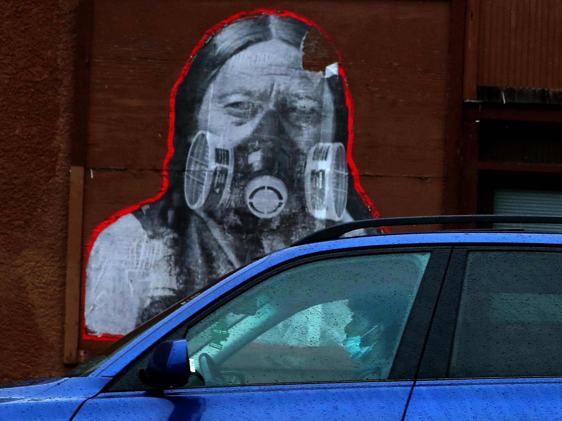 A motorist with a face mask drives by a mural of Native American Chief Sitting Bull wearing breathing apparatus along S. Cedar Avenue near E. 38th Street on April 28, 2020, in Minneapolis.