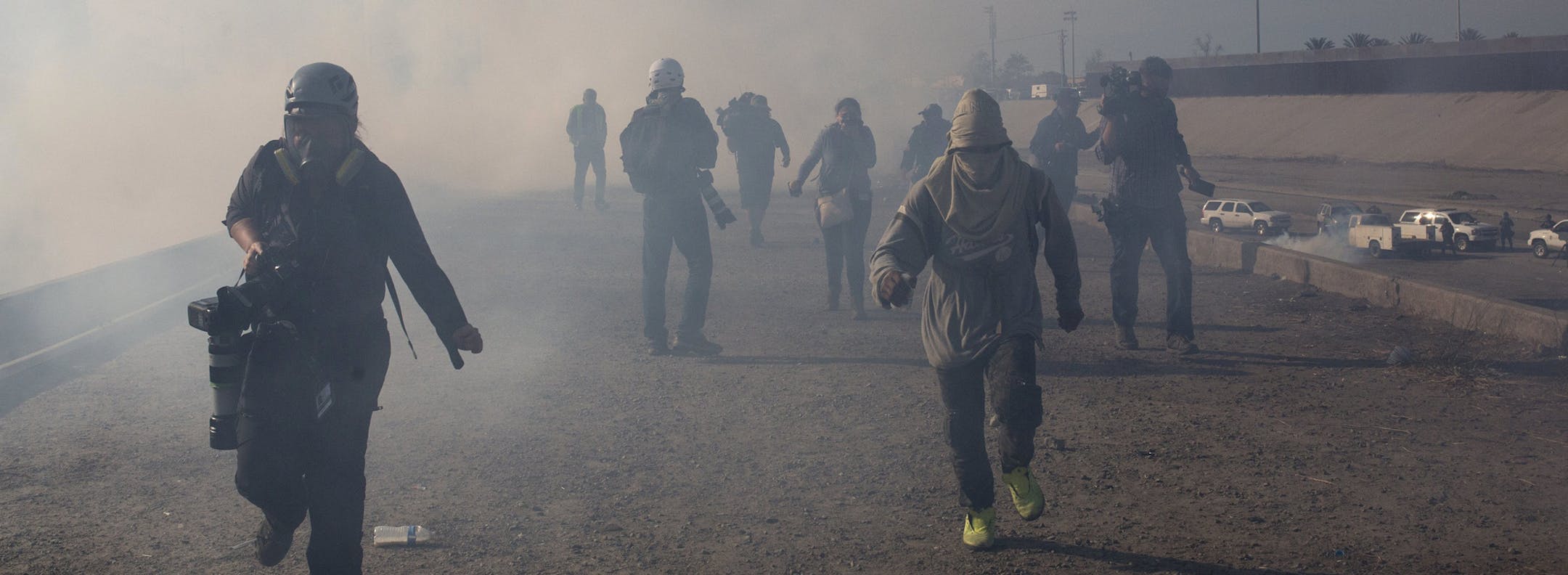 Migrants run from tear gas launched by U.S. agents, amid photojournalists covering the Mexico-U.S. border, after a group of migrants got past Mexican police at the Chaparral crossing in Tijuana, Mexico, Sunday, Nov. 25, 2018. The mayor of Tijuana has declared a humanitarian crisis in his border city and says that he has asked the United Nations for aid to deal with the approximately 5,000 Central American migrants who have arrived in the city. (AP Photo/Rodrigo Abd)