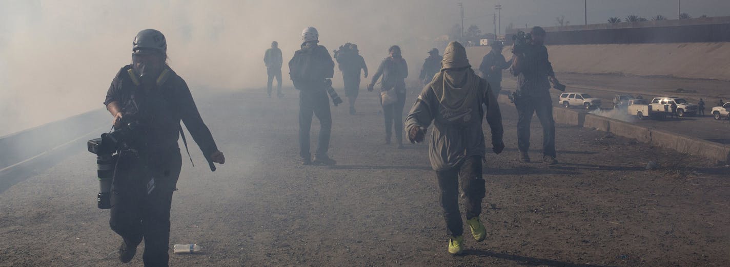 Migrants run from tear gas launched by U.S. agents, amid photojournalists covering the Mexico-U.S. border, after a group of migrants got past Mexican police at the Chaparral crossing in Tijuana, Mexico, Sunday, Nov. 25, 2018. The mayor of Tijuana has declared a humanitarian crisis in his border city and says that he has asked the United Nations for aid to deal with the approximately 5,000 Central American migrants who have arrived in the city. (AP Photo/Rodrigo Abd)